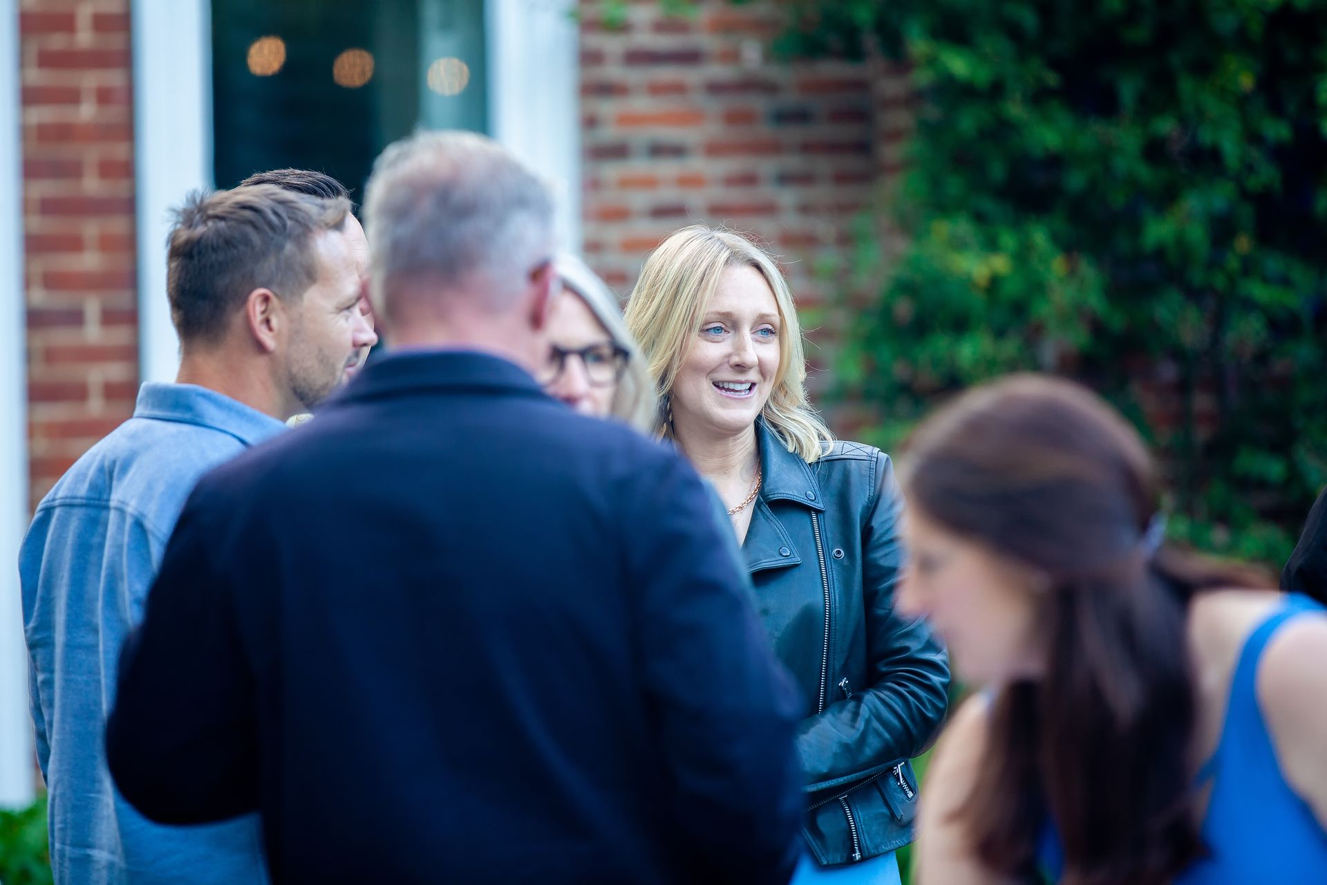 People socializing outdoors, woman smiling, brick building in background.
