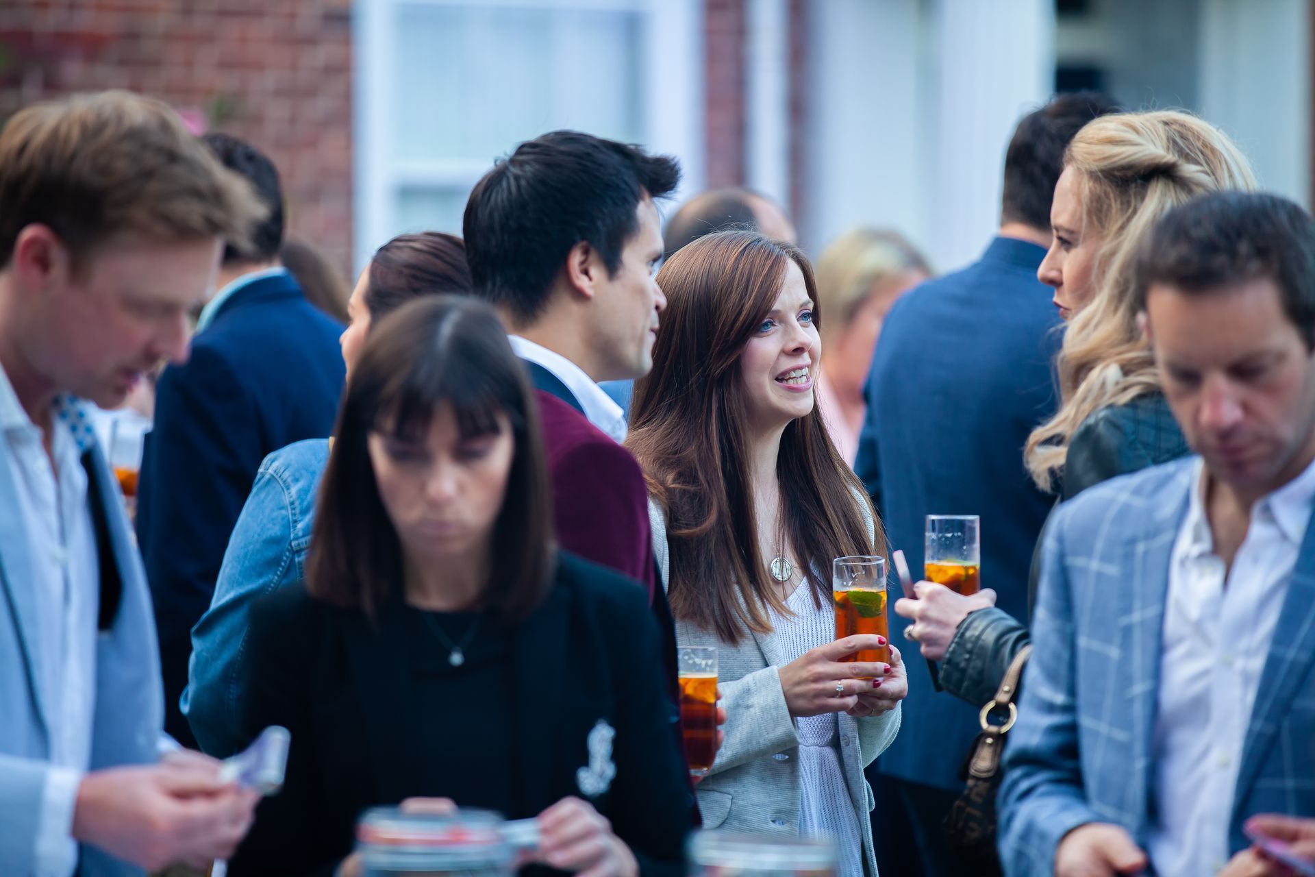 People at an outdoor party, some holding drinks. Various expressions and clothing styles visible.