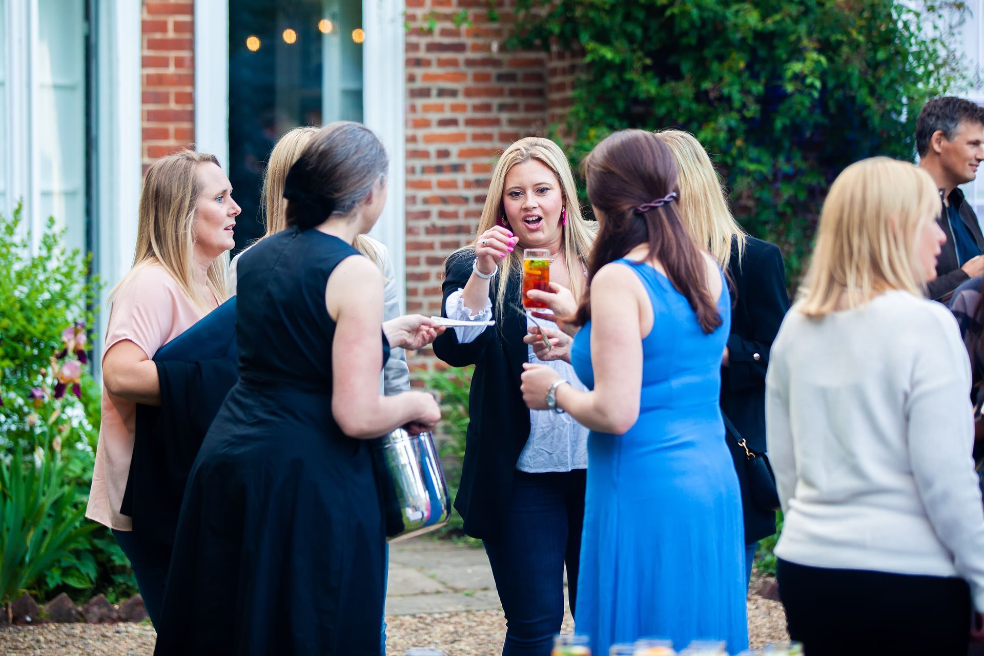 A group of women socializing outdoors, one holding a drink. Brick building in the background.