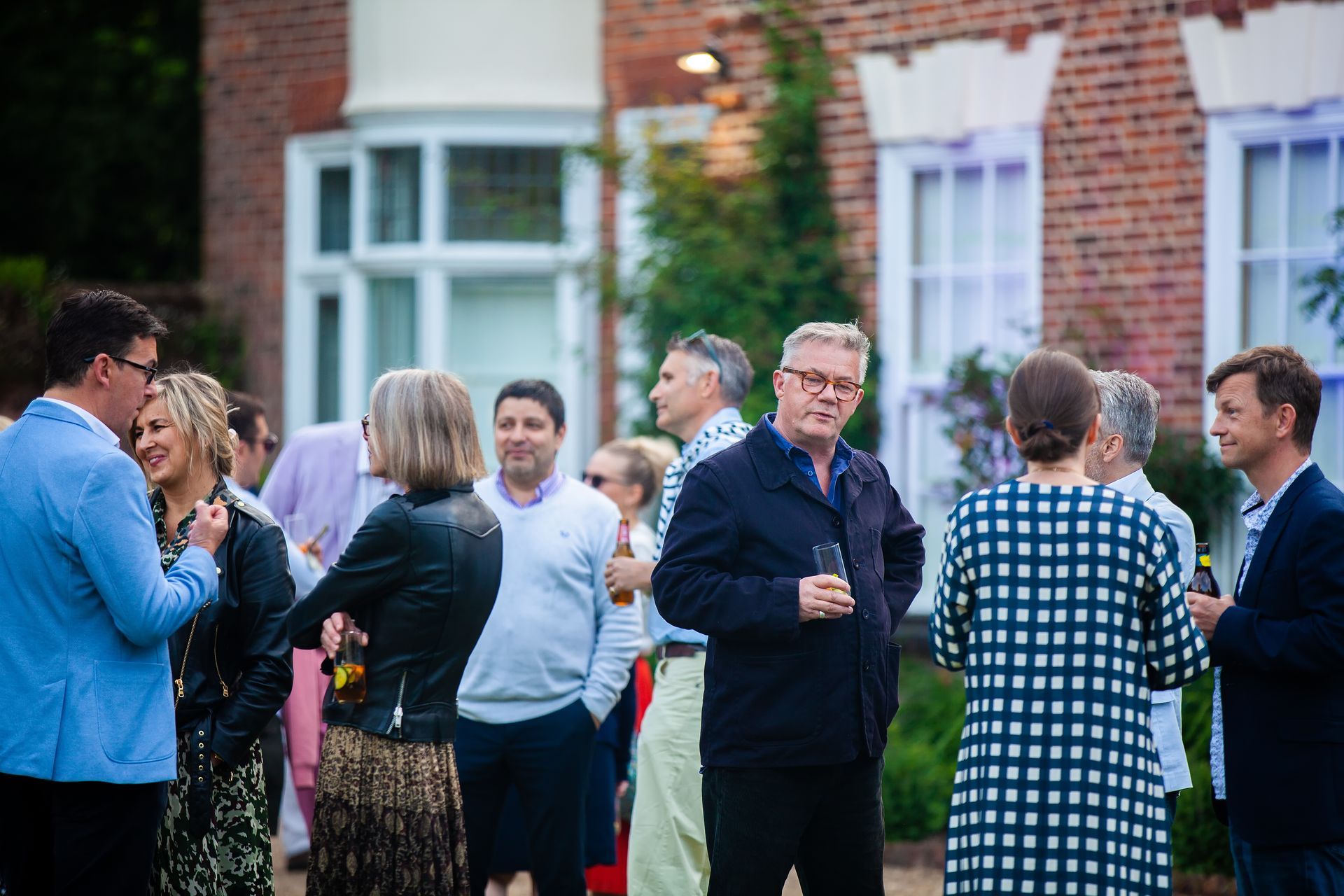 People mingling outside a brick building at a social gathering.
