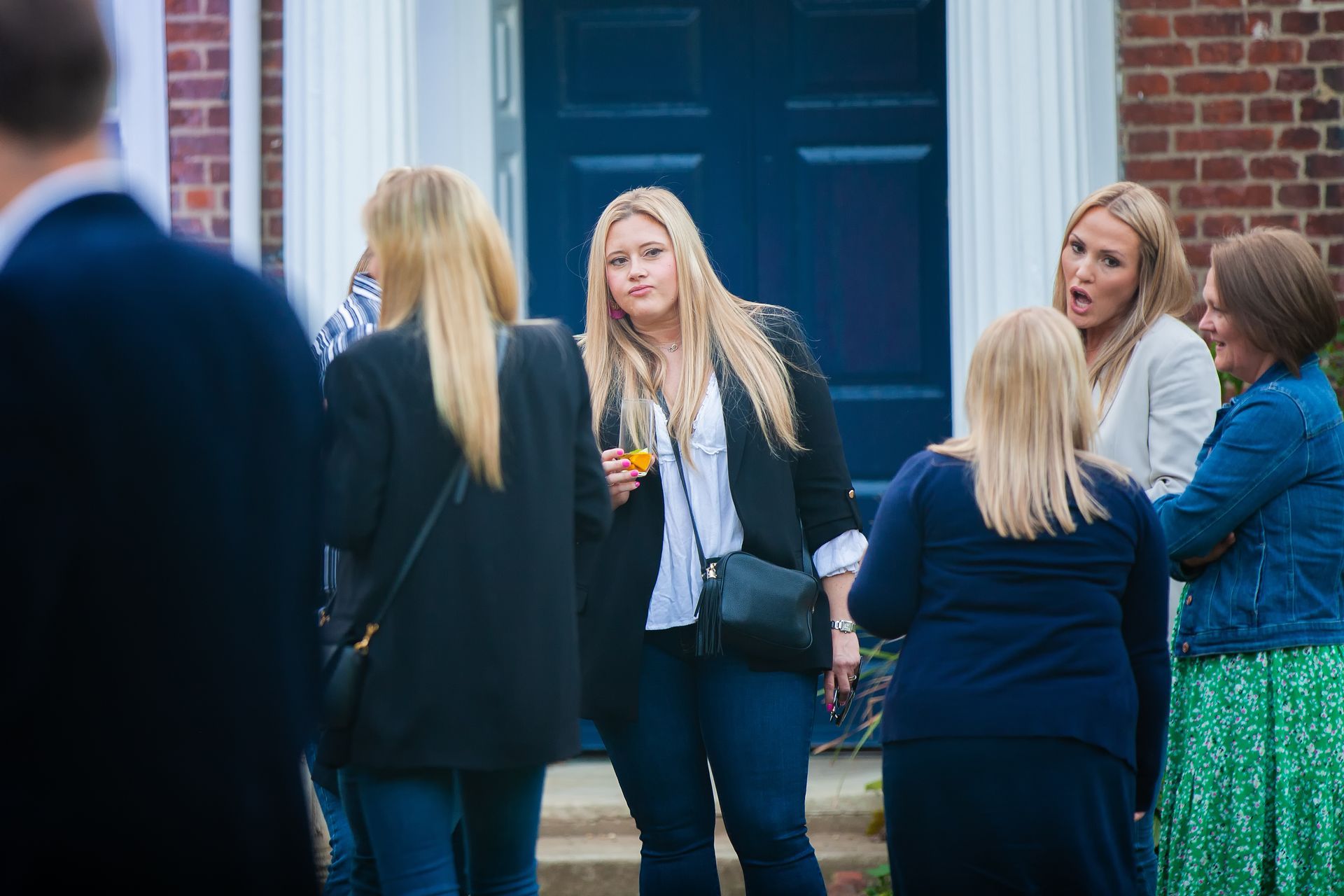 Group of women chatting outside a brick building with a blue door. Some are holding drinks.