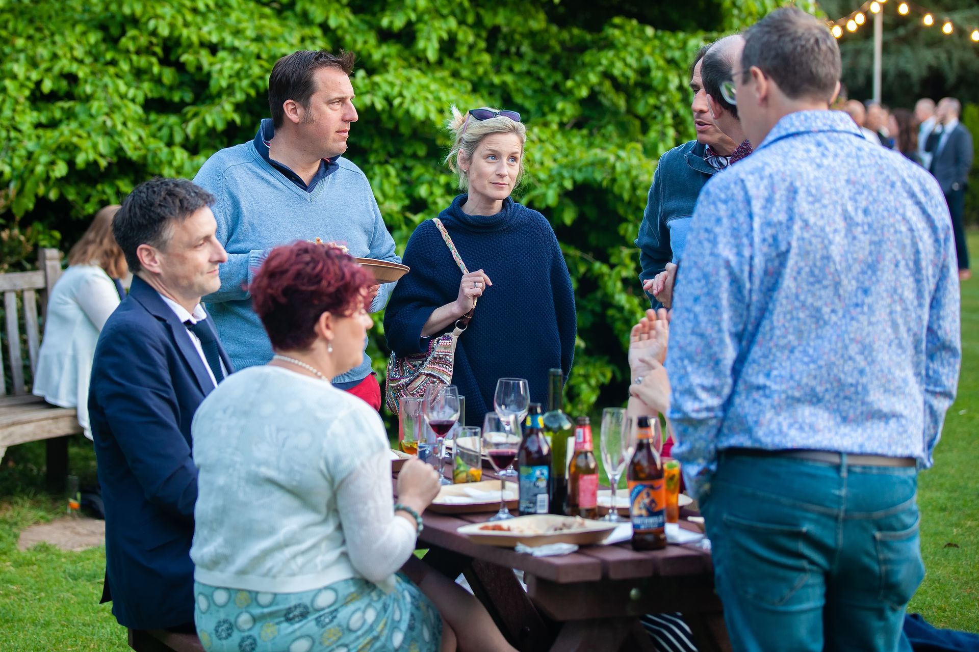 People gathered around a picnic table outdoors, conversing and enjoying a meal.