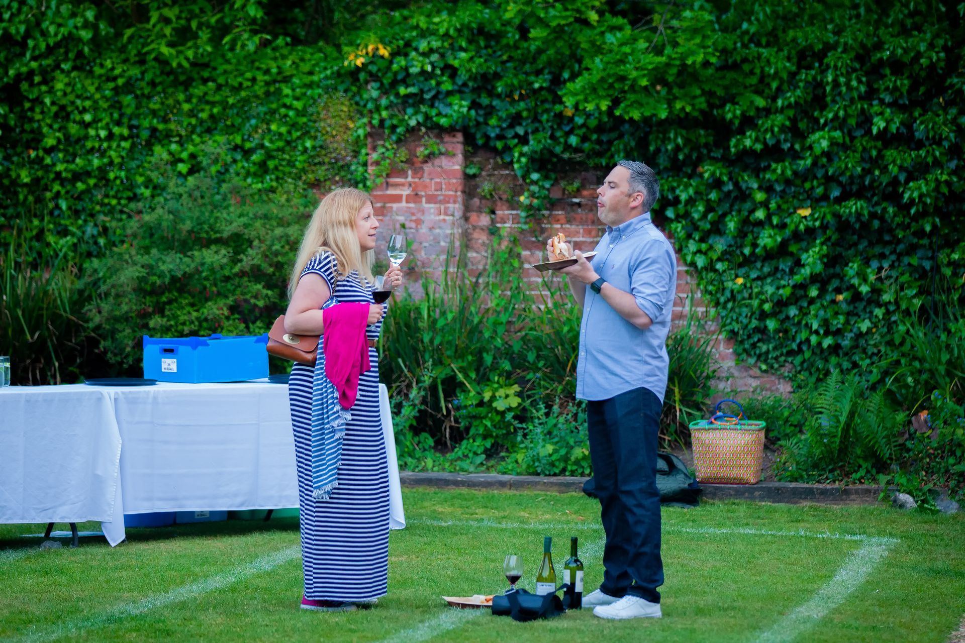 Woman in striped dress, man with candles, outdoors. Green lawn, party setting.