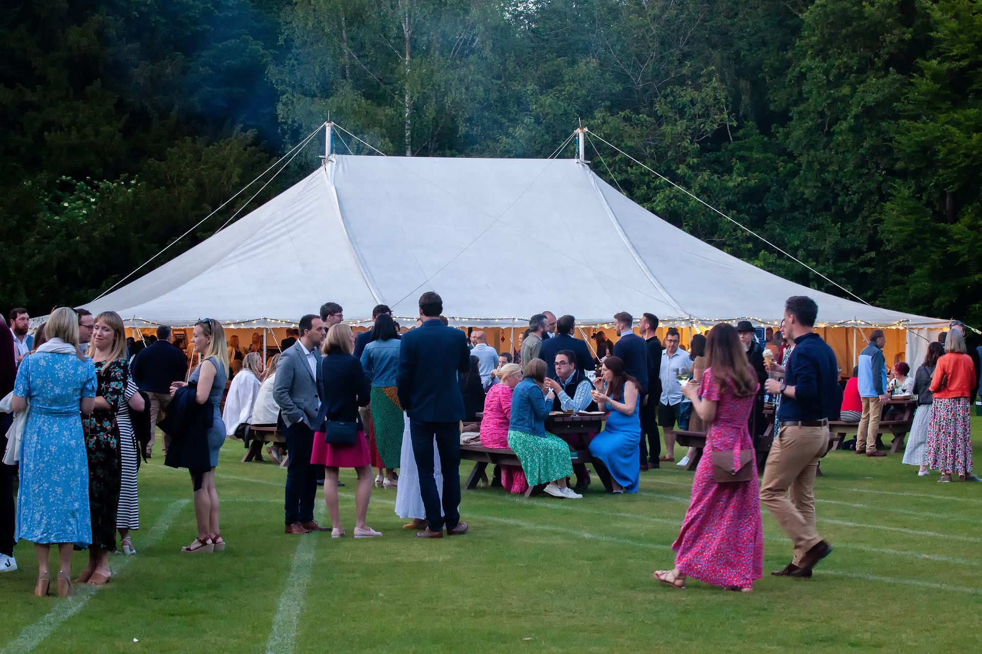 People at outdoor party under a white tent, on a green lawn.