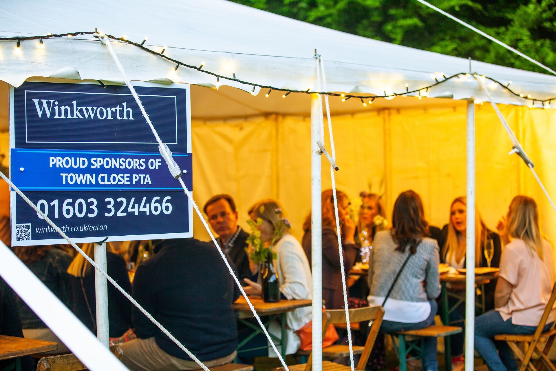 People seated at tables under a tent, a sign for Winkworth real estate visible.