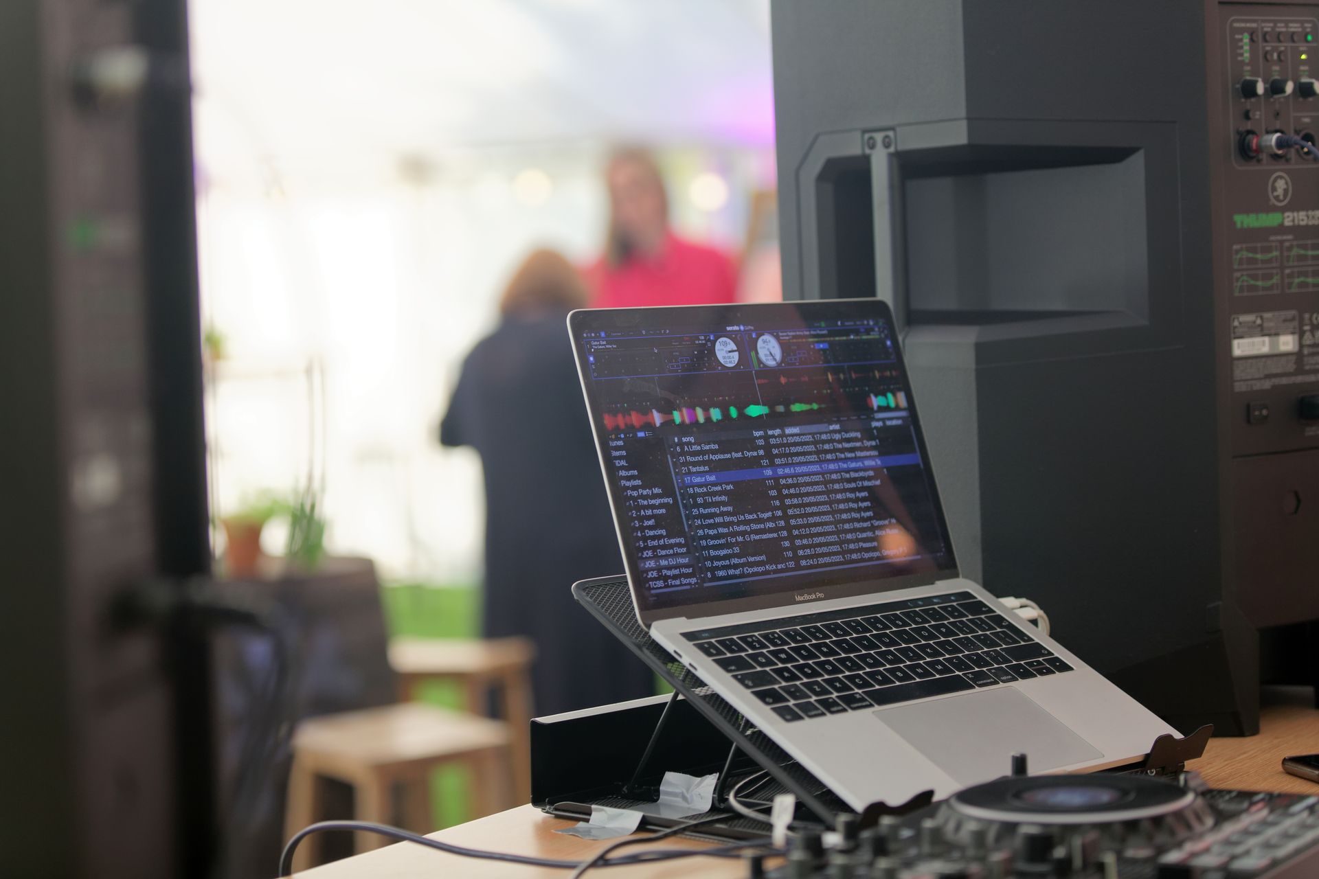 Laptop playing music on a stand at a party with blurry people in the background.