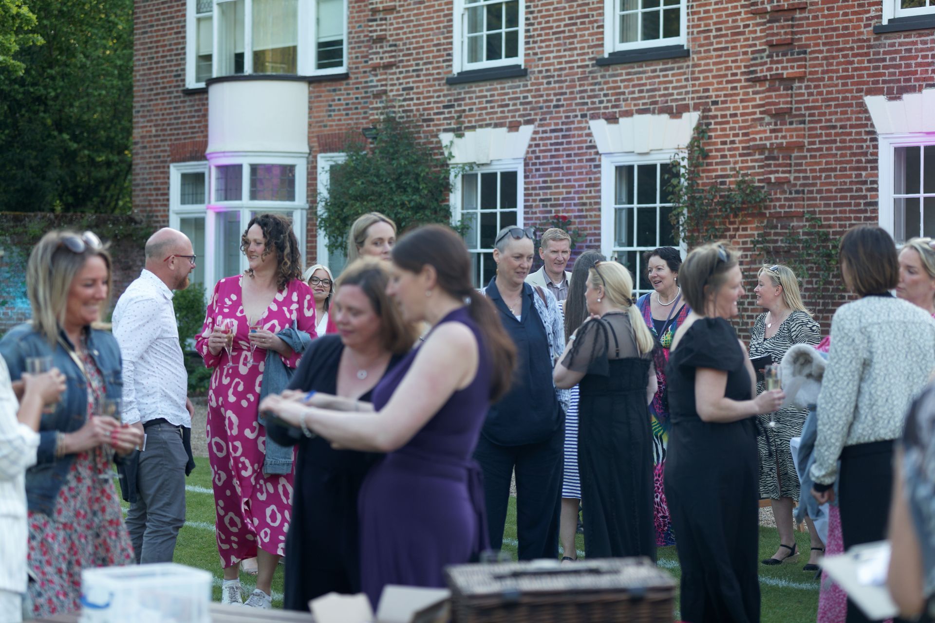 People gathered on a lawn in front of a brick building. Evening reception with attendees in dresses and suits.