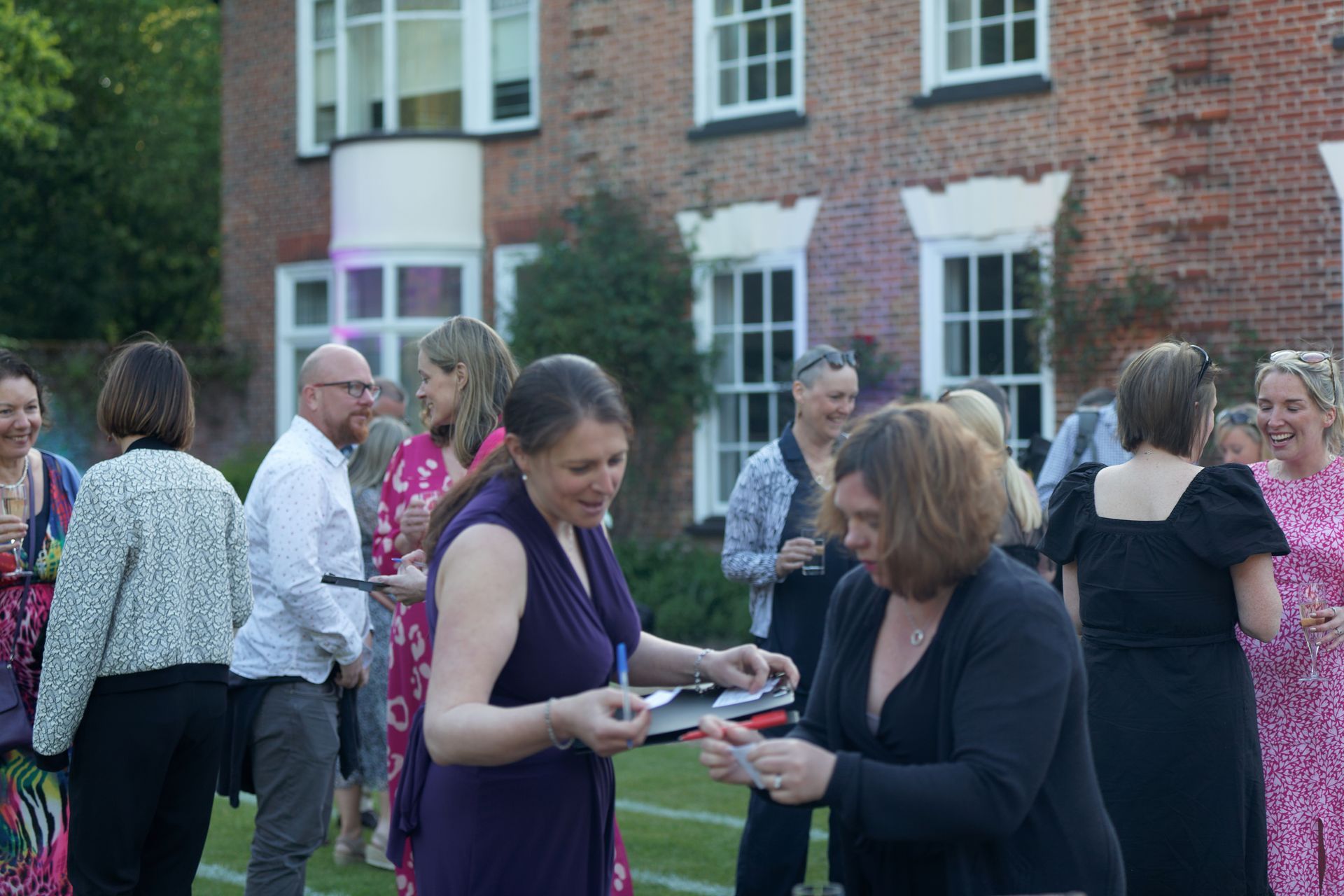 Two women signing documents outdoors near a brick building. People are in the background.