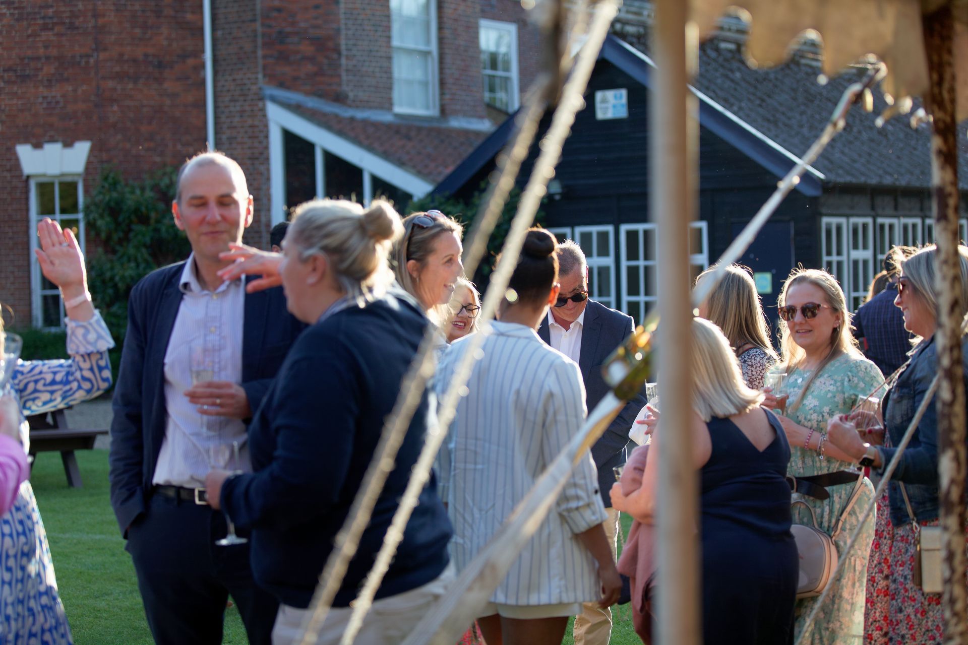 People socializing outdoors, some holding drinks, with a building in the background.