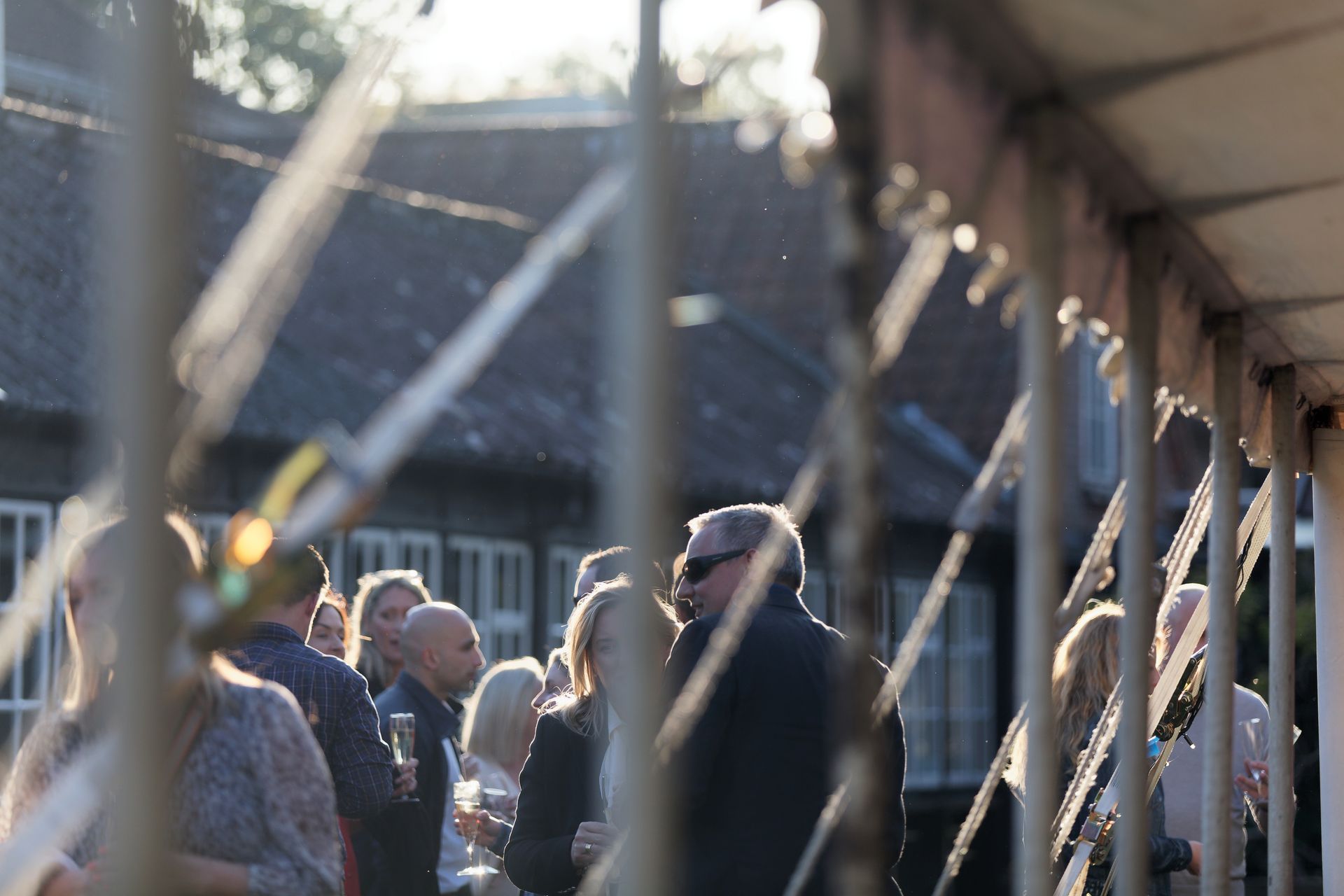 Group of people at an outdoor event, blurred by a fence in front.