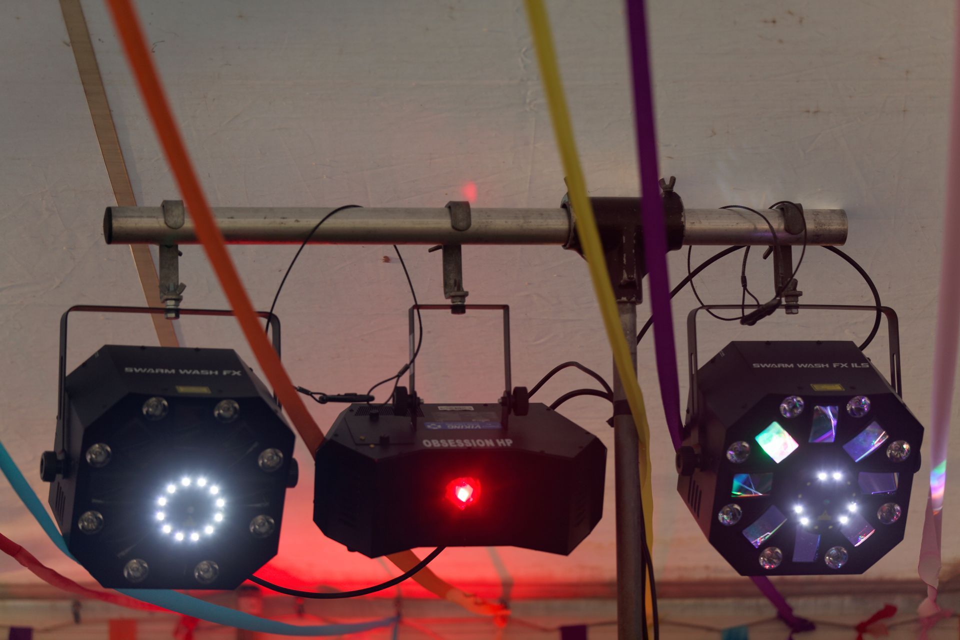 Three stage lights on a bar, with colorful ribbons hanging.