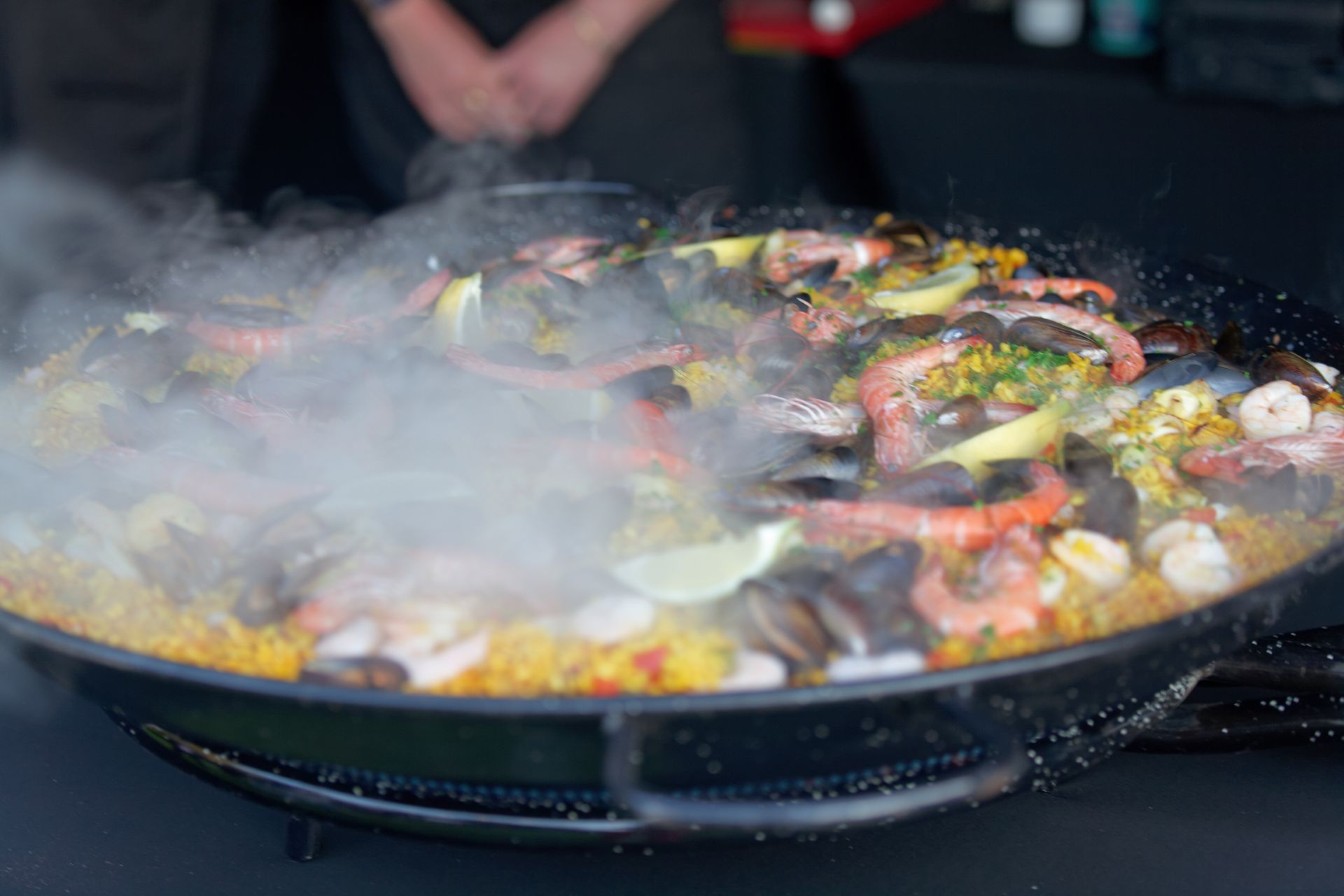Paella cooking in a large pan, with steam rising. Seafood and rice visible.