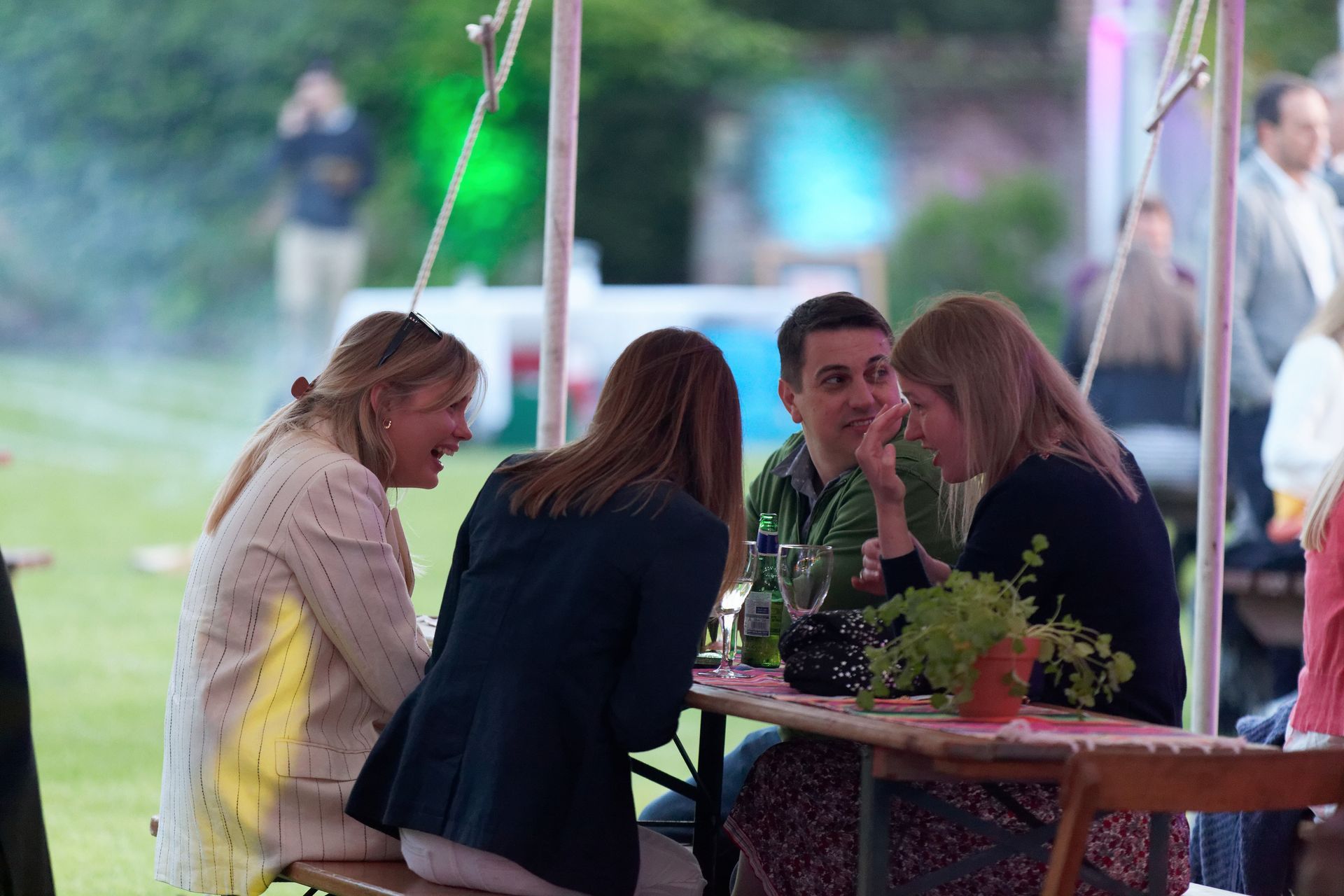 Four people sitting at a table outside, laughing and talking at an event.