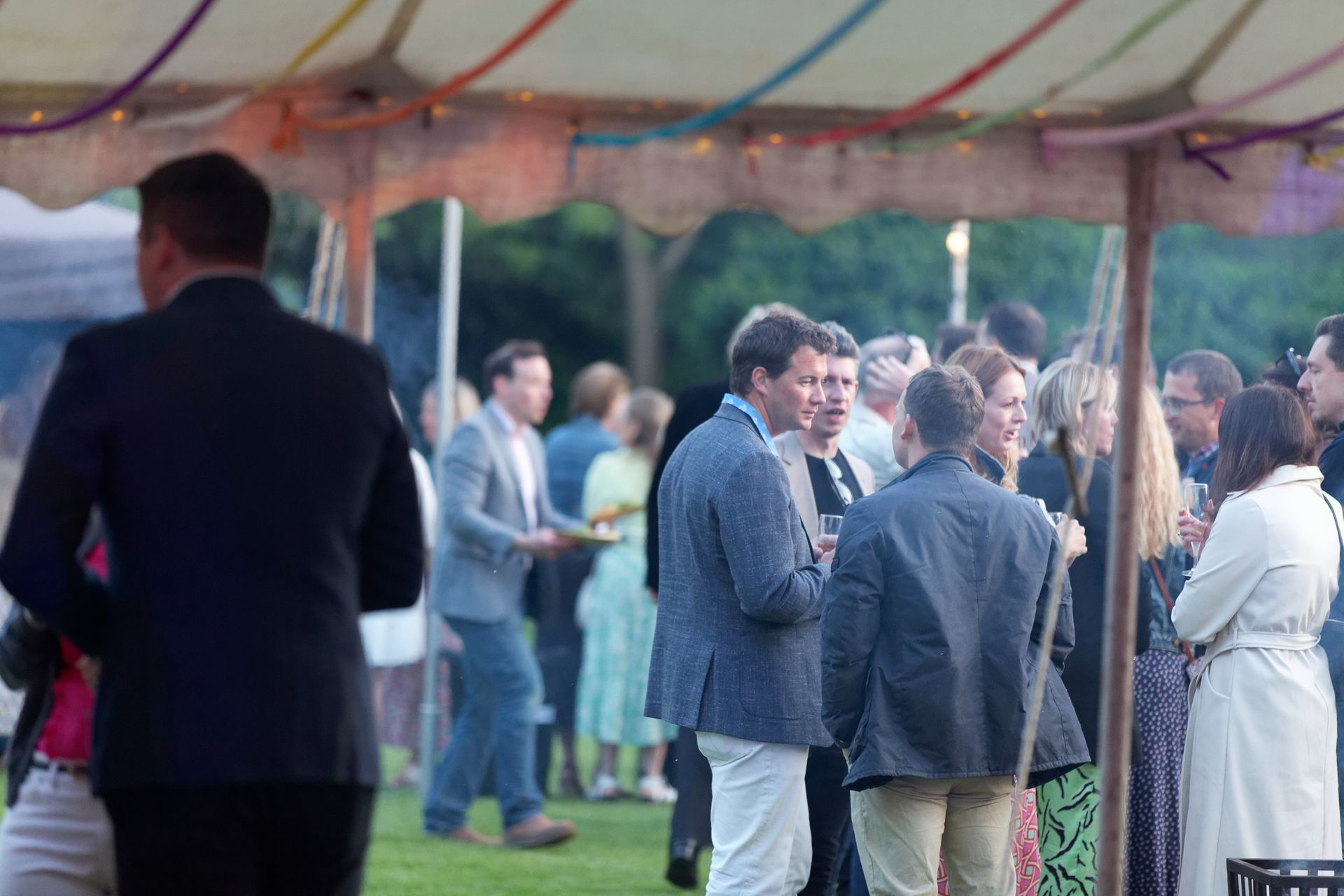 People socializing at an outdoor event under a tent.