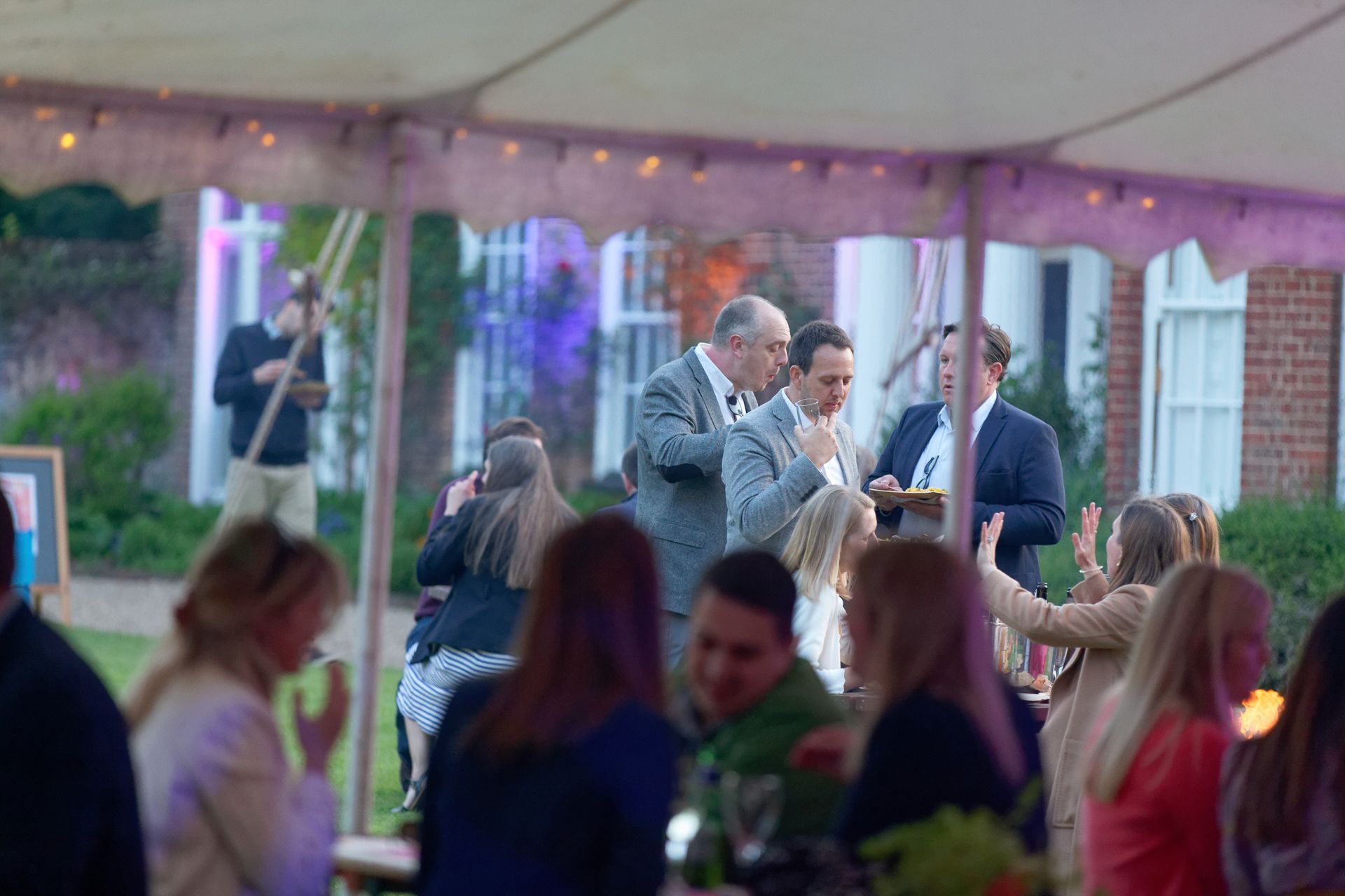 People gathered under a tent at an outdoor event, with some interacting and others watching.