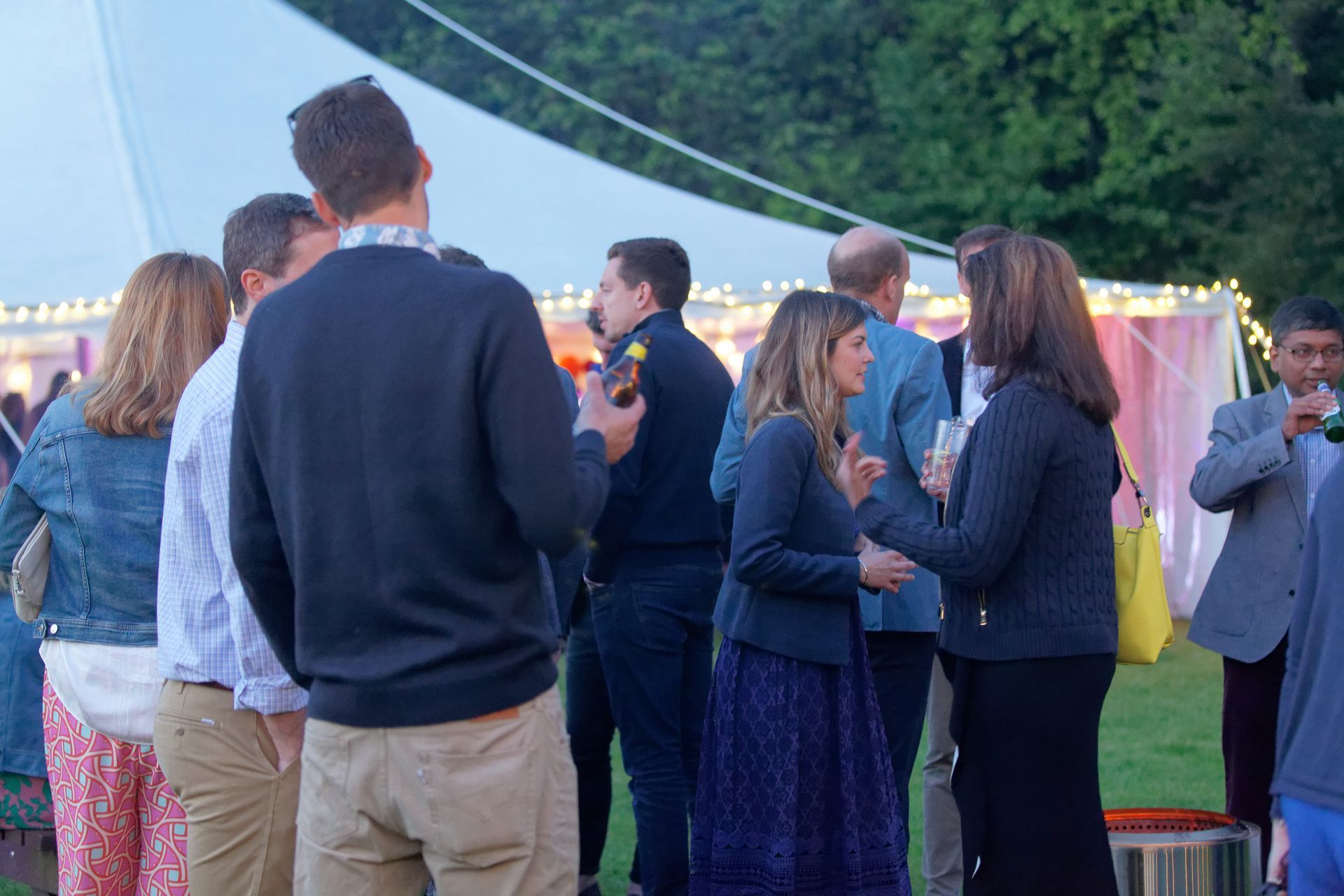 People socializing outdoors at a party, near a white tent.