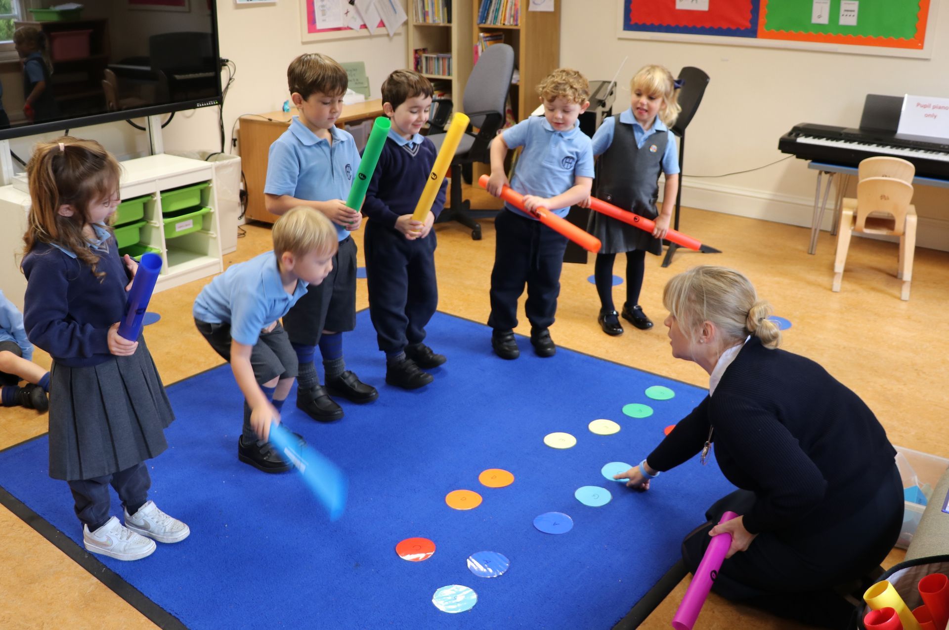 Children and teacher playing a musical game on a mat with colorful circles, using batons.