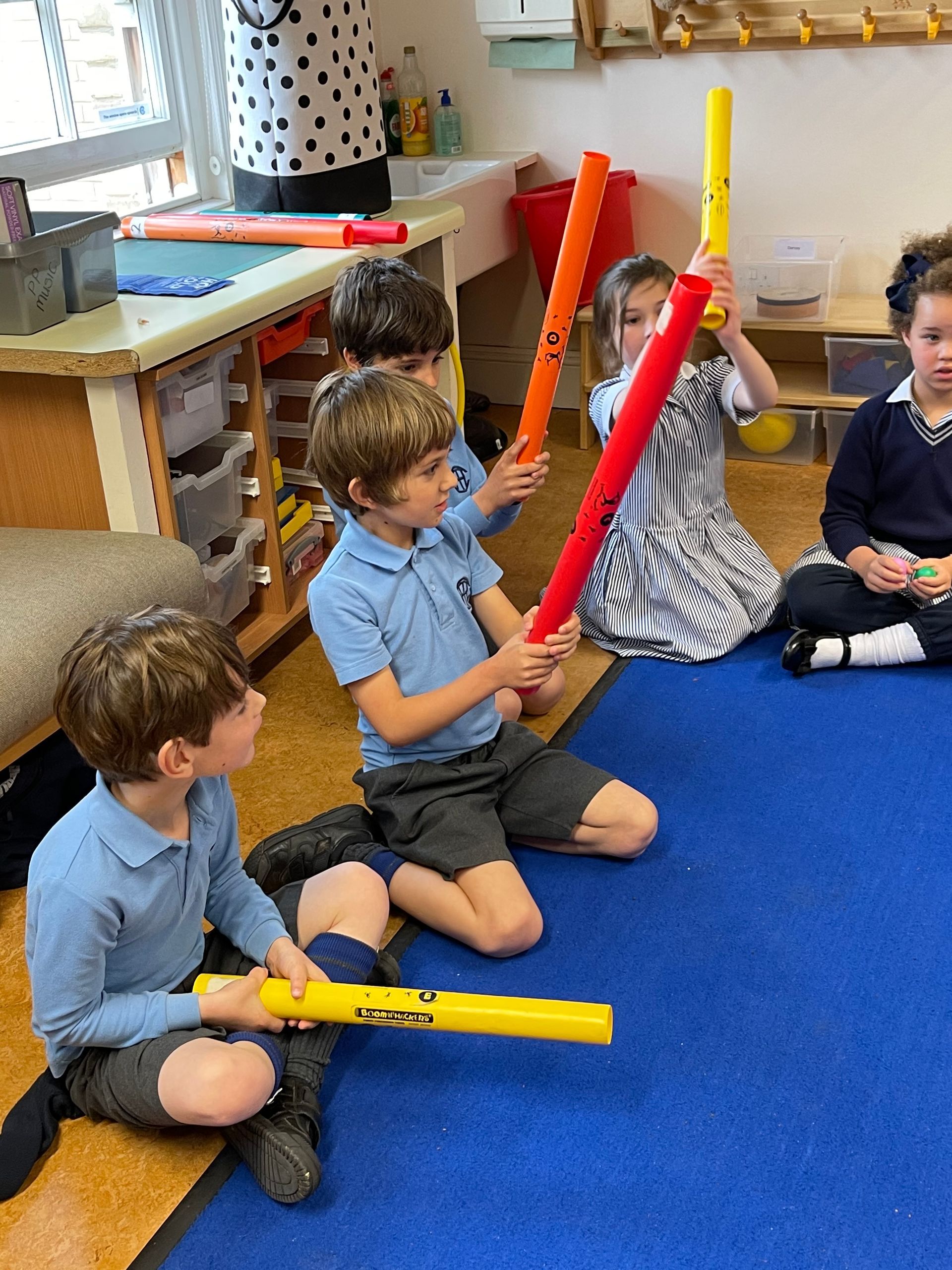 Children in a classroom holding colorful, long musical tubes.