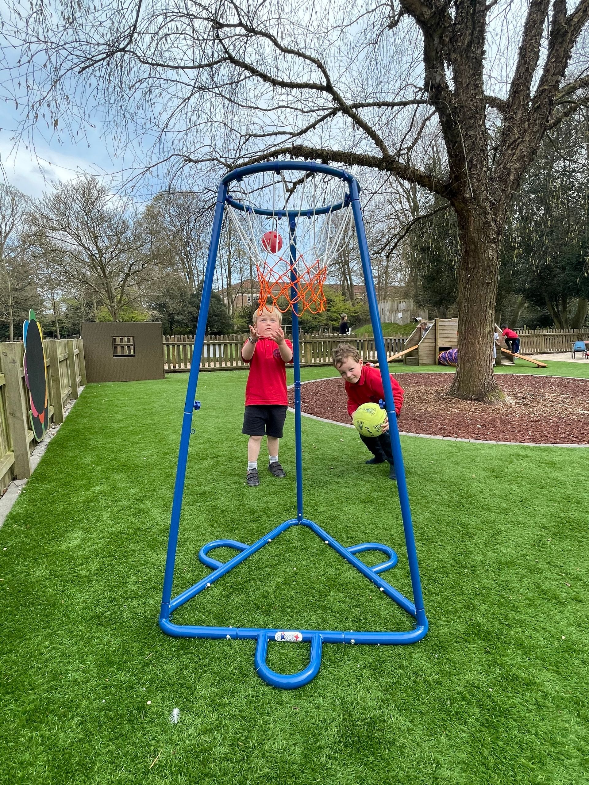 Two kids play with balls at a blue frame in a grassy yard.