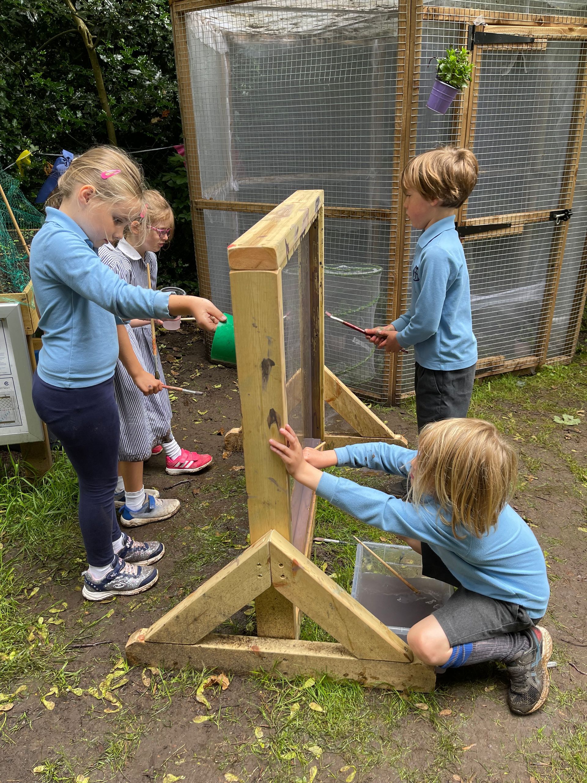 Children interacting with a wooden frame screen outdoors. They are touching and looking at it.