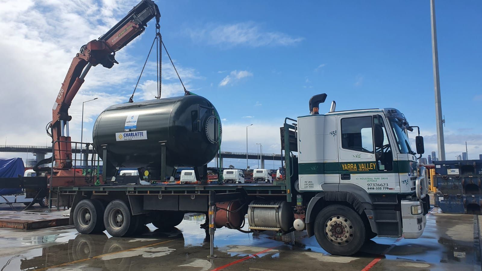 A large black tank is being lifted by a crane on the back of a truck.