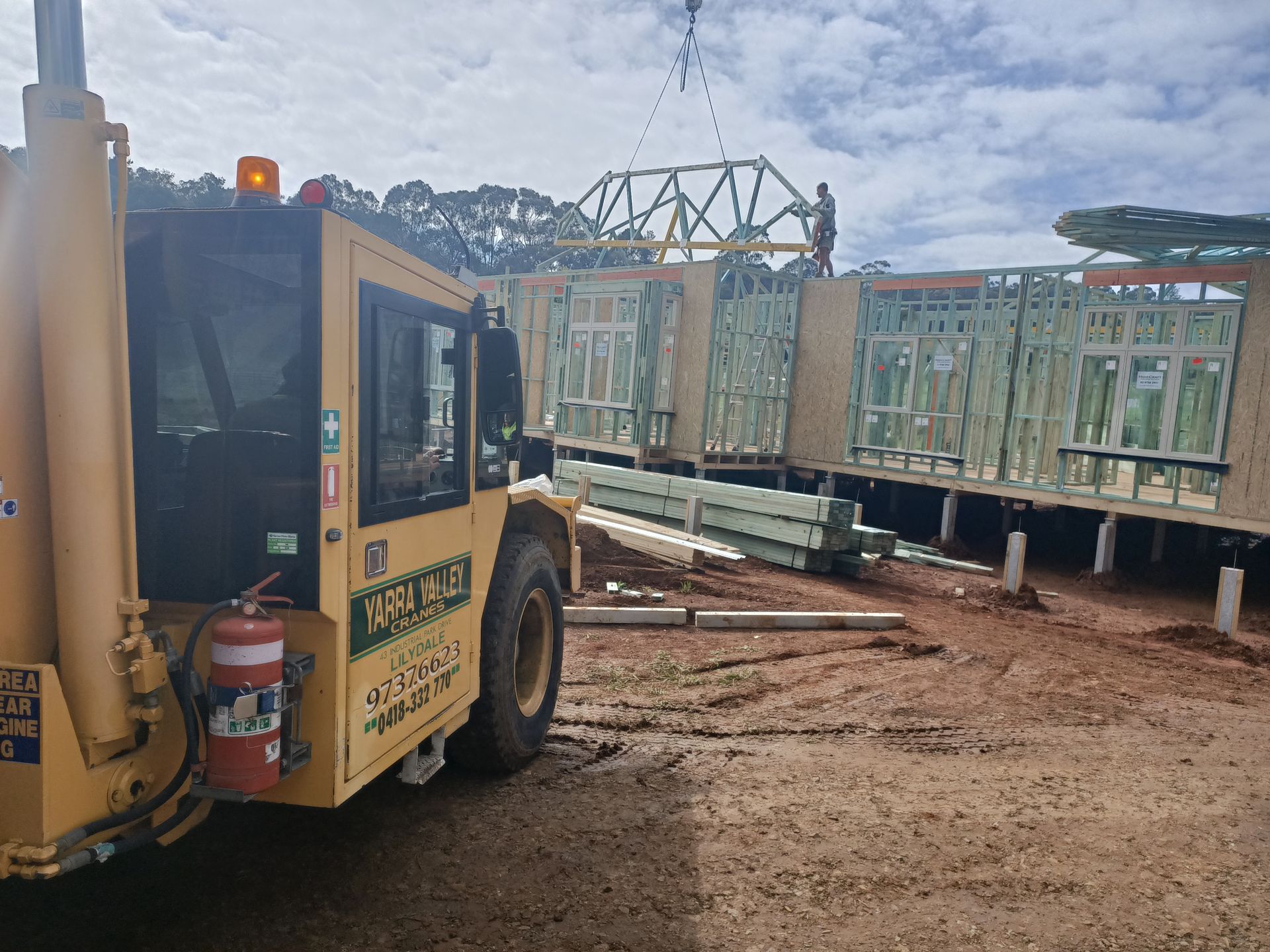 A yellow truck is driving down a dirt road next to a building under construction.