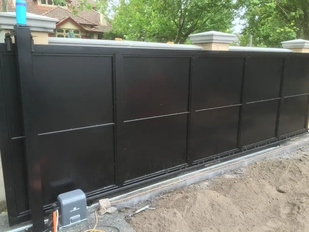 A black sliding gate is sitting in the dirt next to a house.