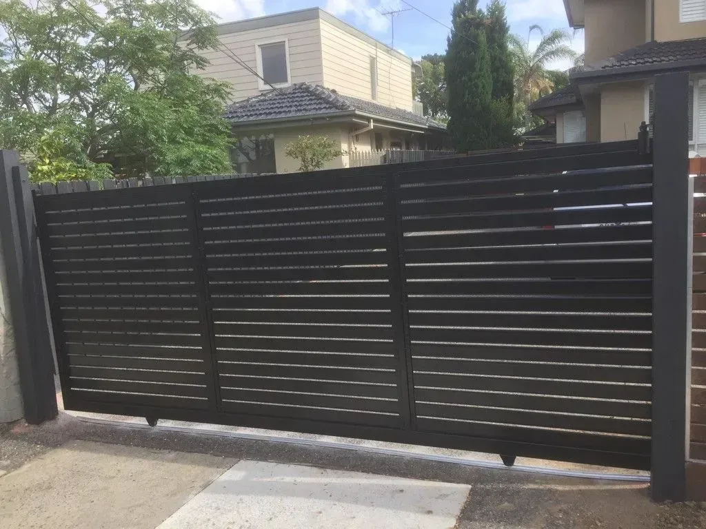 A black sliding gate is sitting in front of a house.
