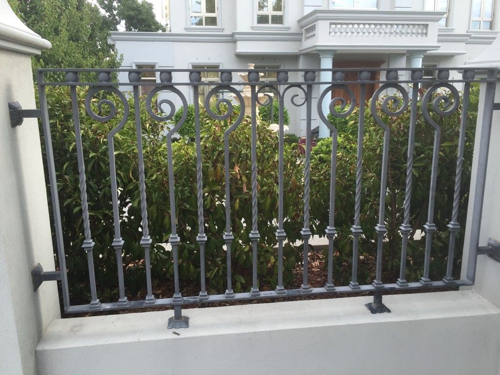 A wrought iron fence is surrounded by bushes in front of a house