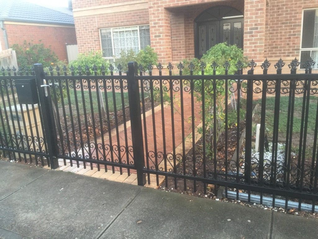 A black metal fence surrounds a brick house
