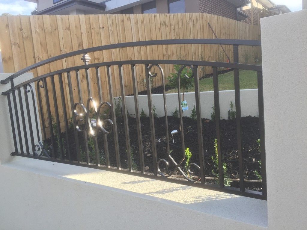 A wrought iron fence with a wooden fence in the background
