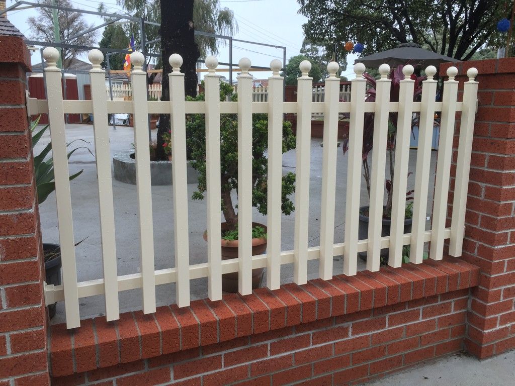 A white picket fence surrounds a brick wall