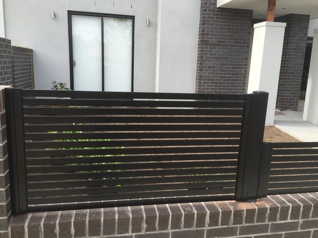 A black fence surrounds a brick wall in front of a house