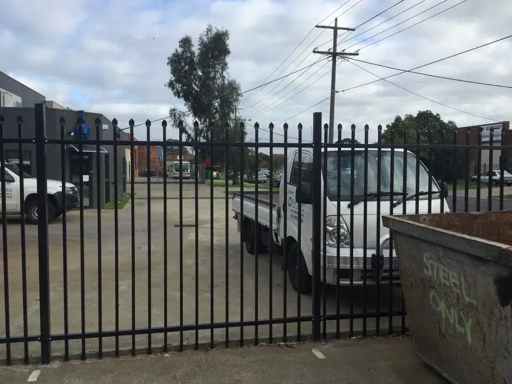 A white truck is parked behind a metal fence.