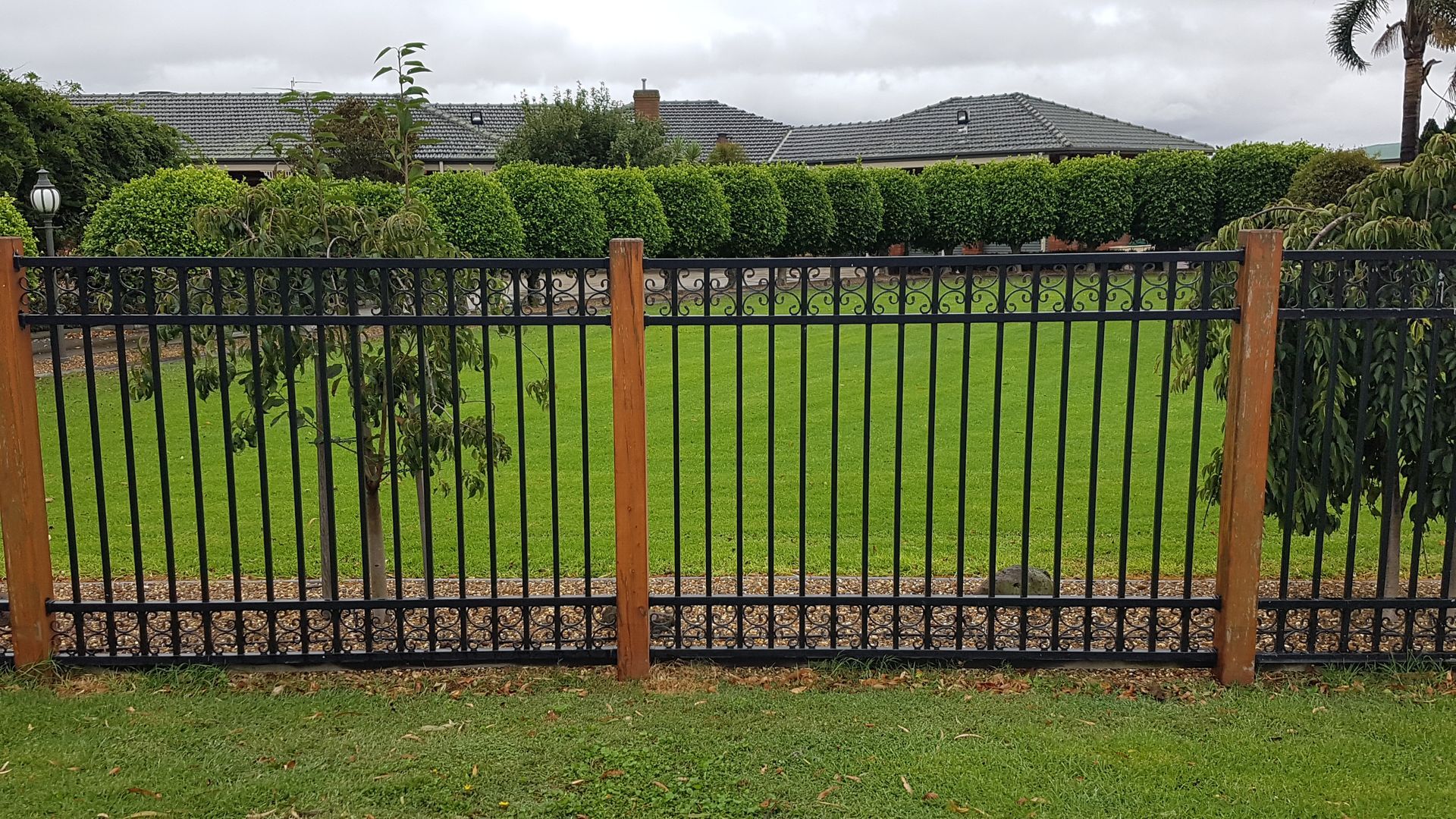 A metal fence surrounds a lush green field in front of a house.