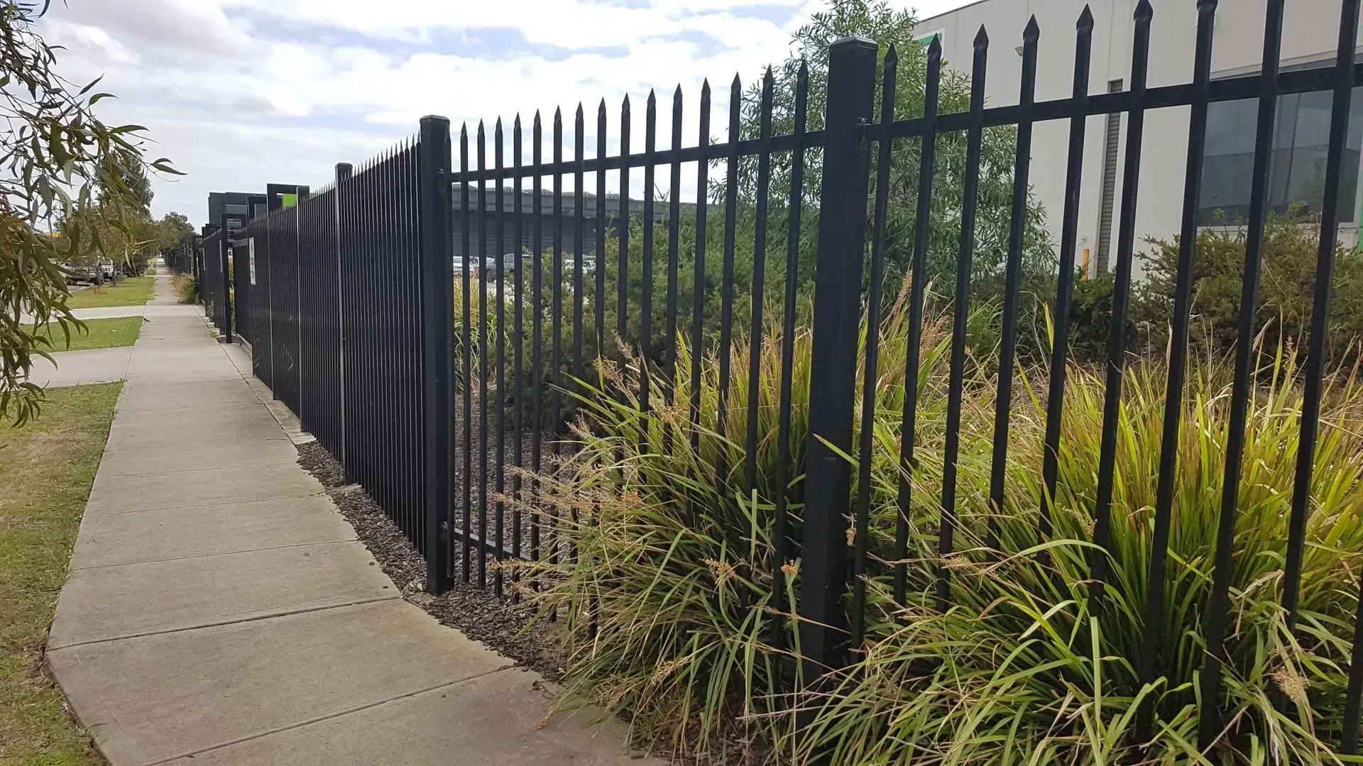 A black metal fence along a sidewalk next to a grassy area.