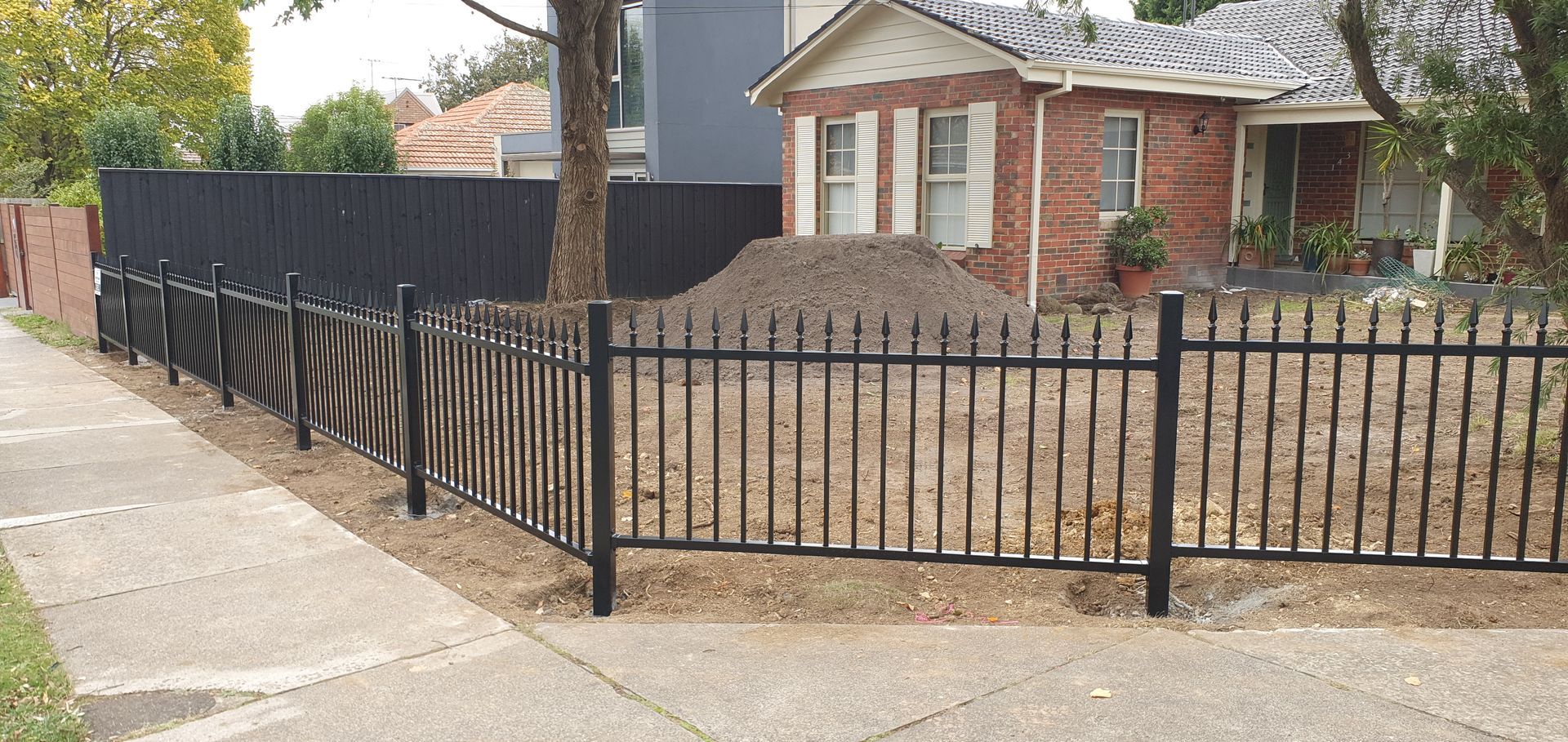 A black fence is surrounding a brick house.