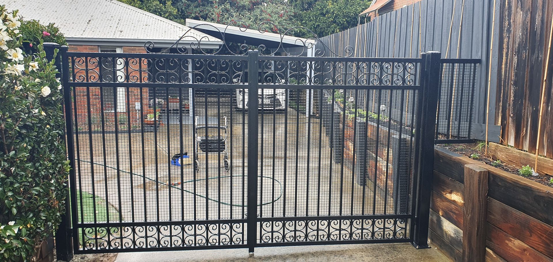 A black wrought iron gate is sitting next to a wooden fence.