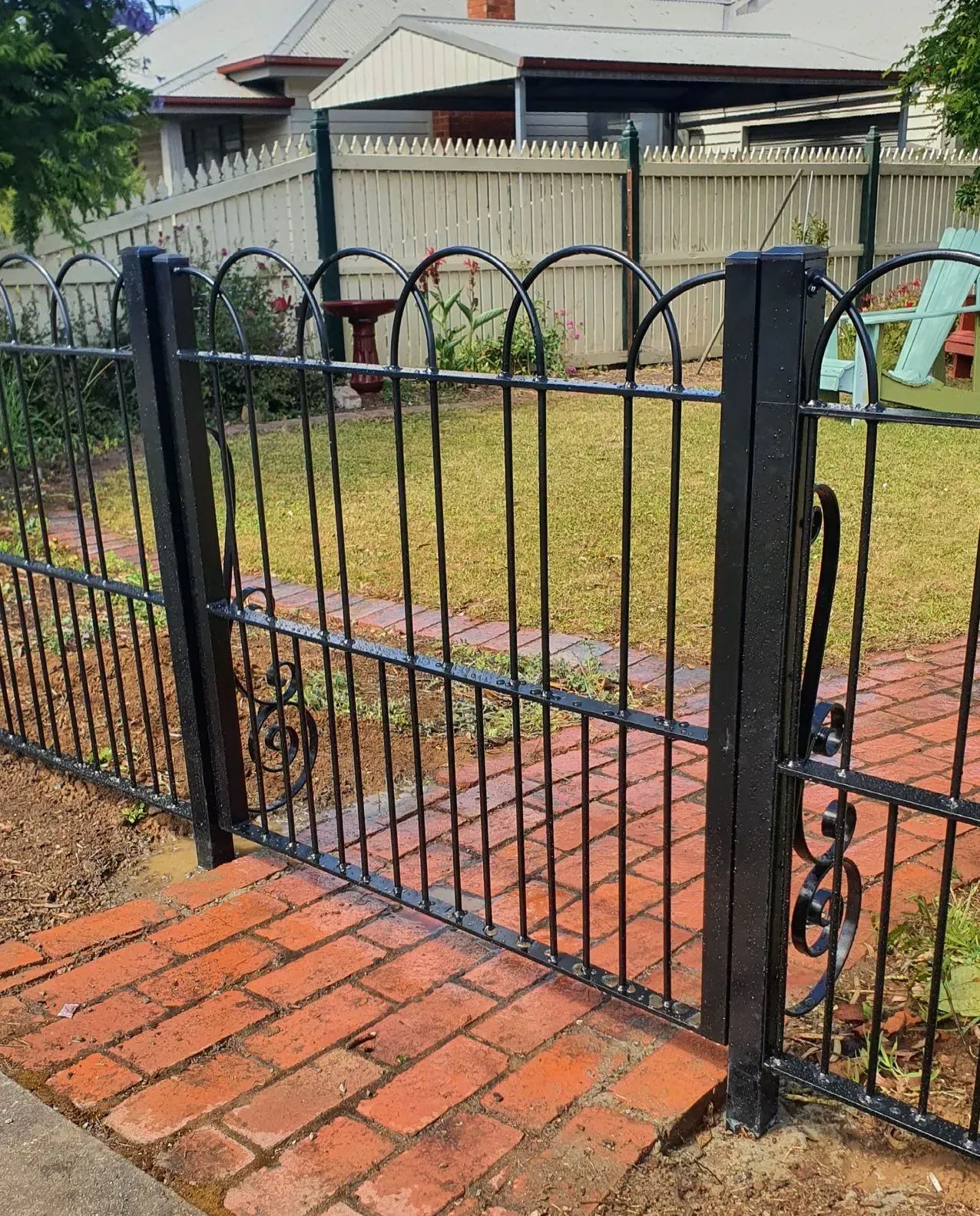 A black wrought iron fence with a brick walkway behind it.