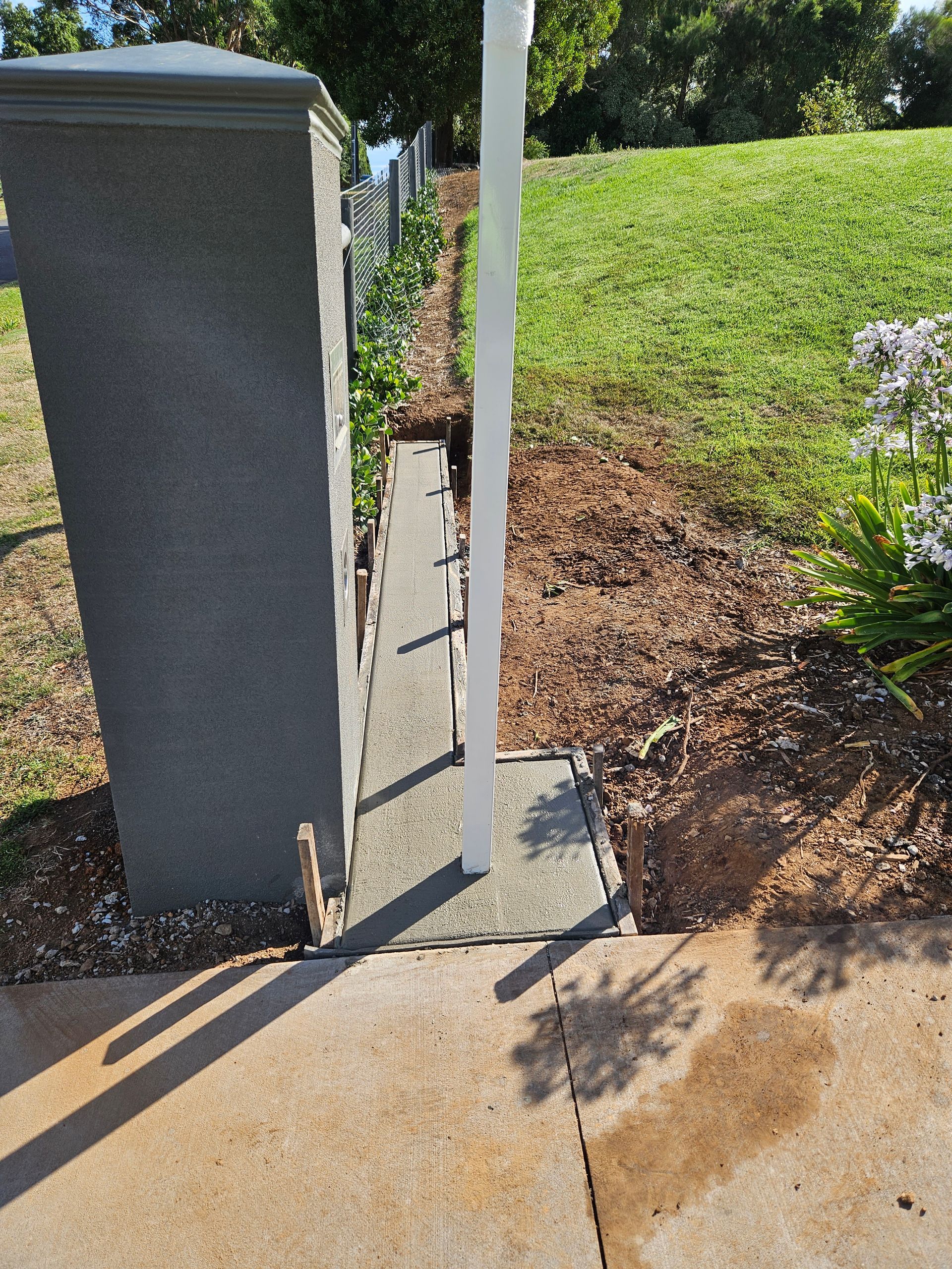 A concrete post is sitting on a sidewalk next to a grassy field.