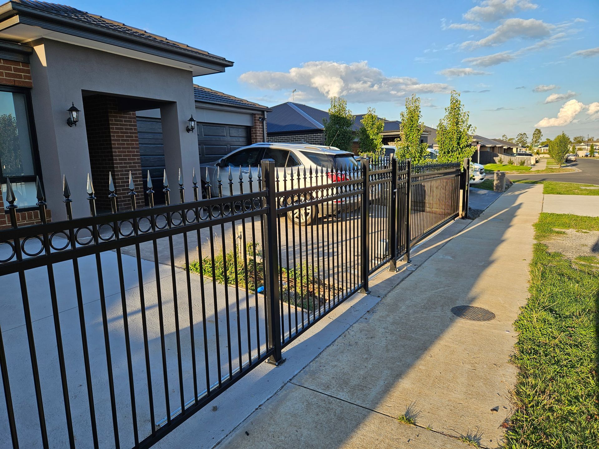 A black wrought iron fence surrounds a house in a residential area.