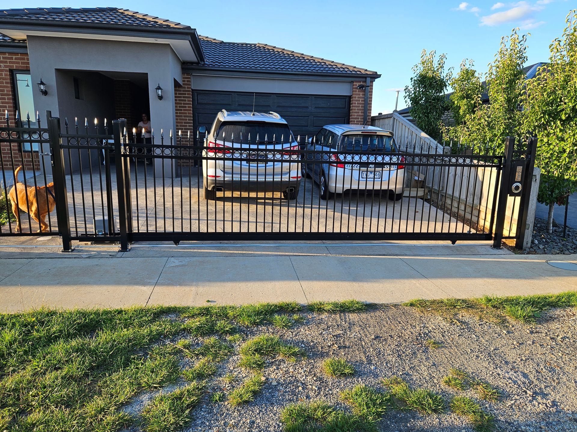 Two cars are parked in a driveway behind a wrought iron gate.