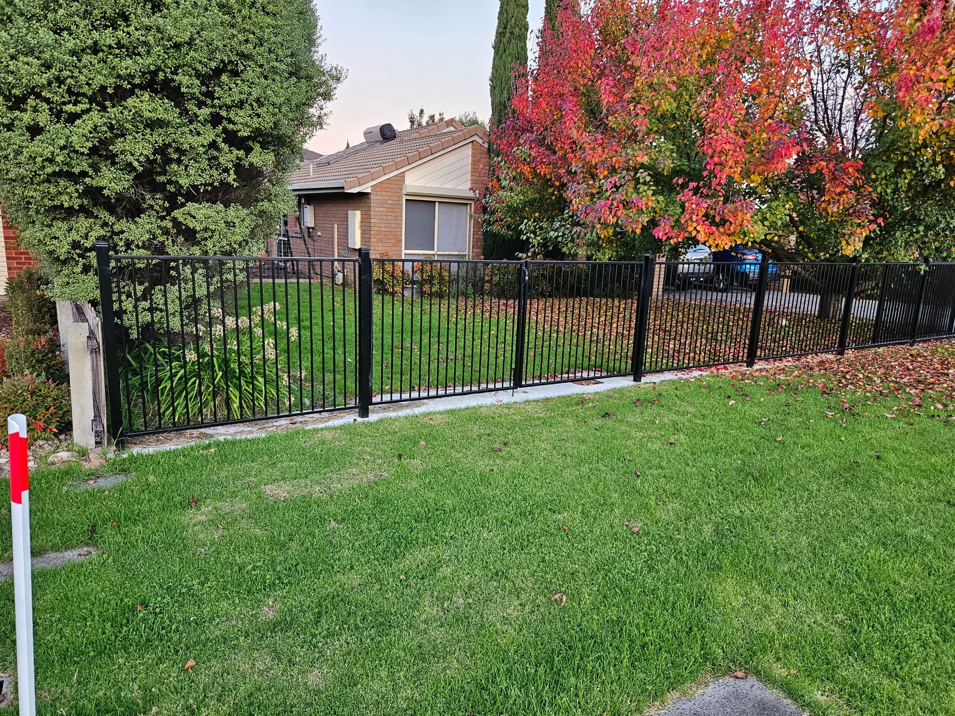 A fence surrounds a lush green lawn in front of a house.