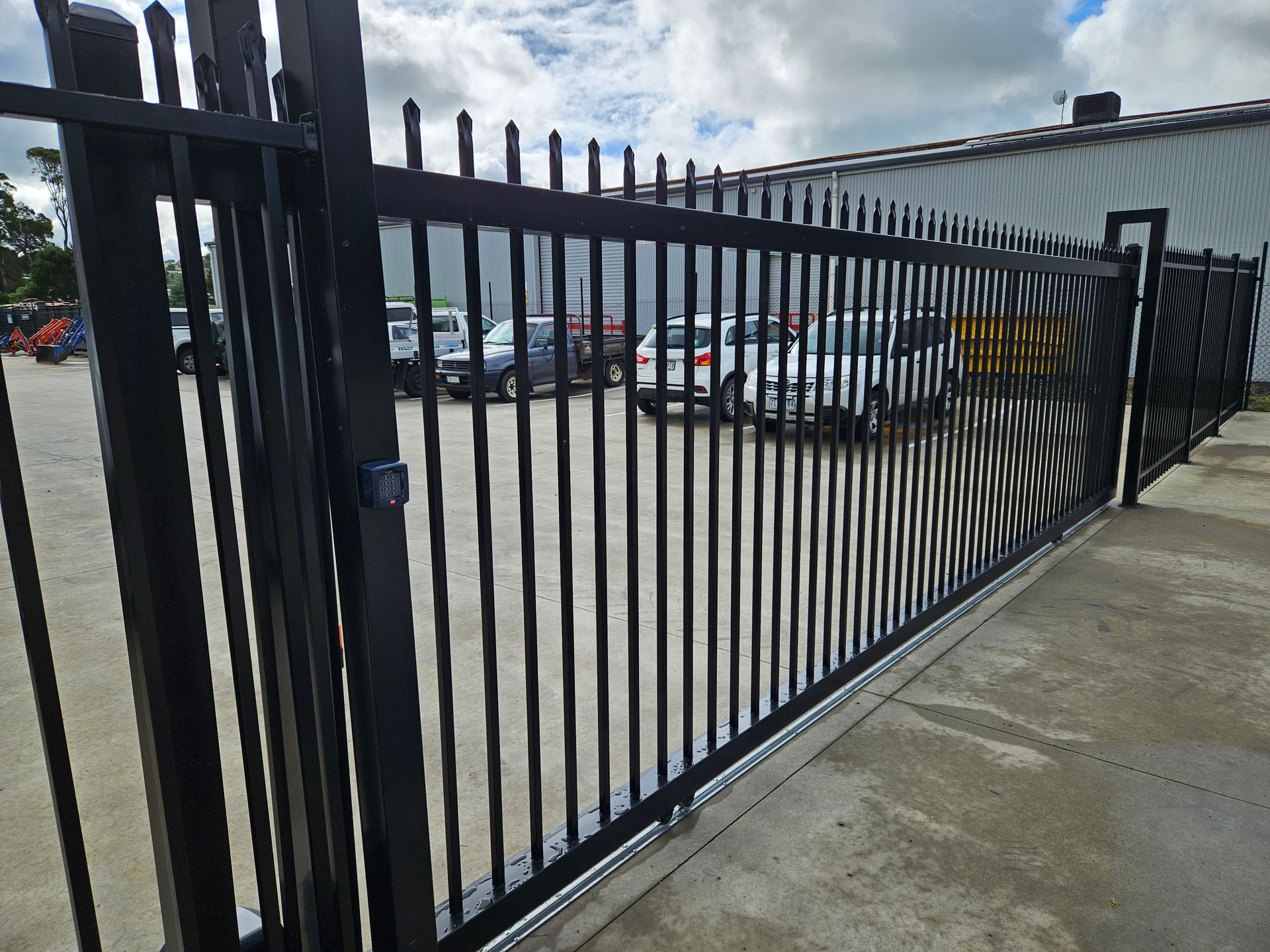 A black fence is surrounding a parking lot with cars parked behind it.