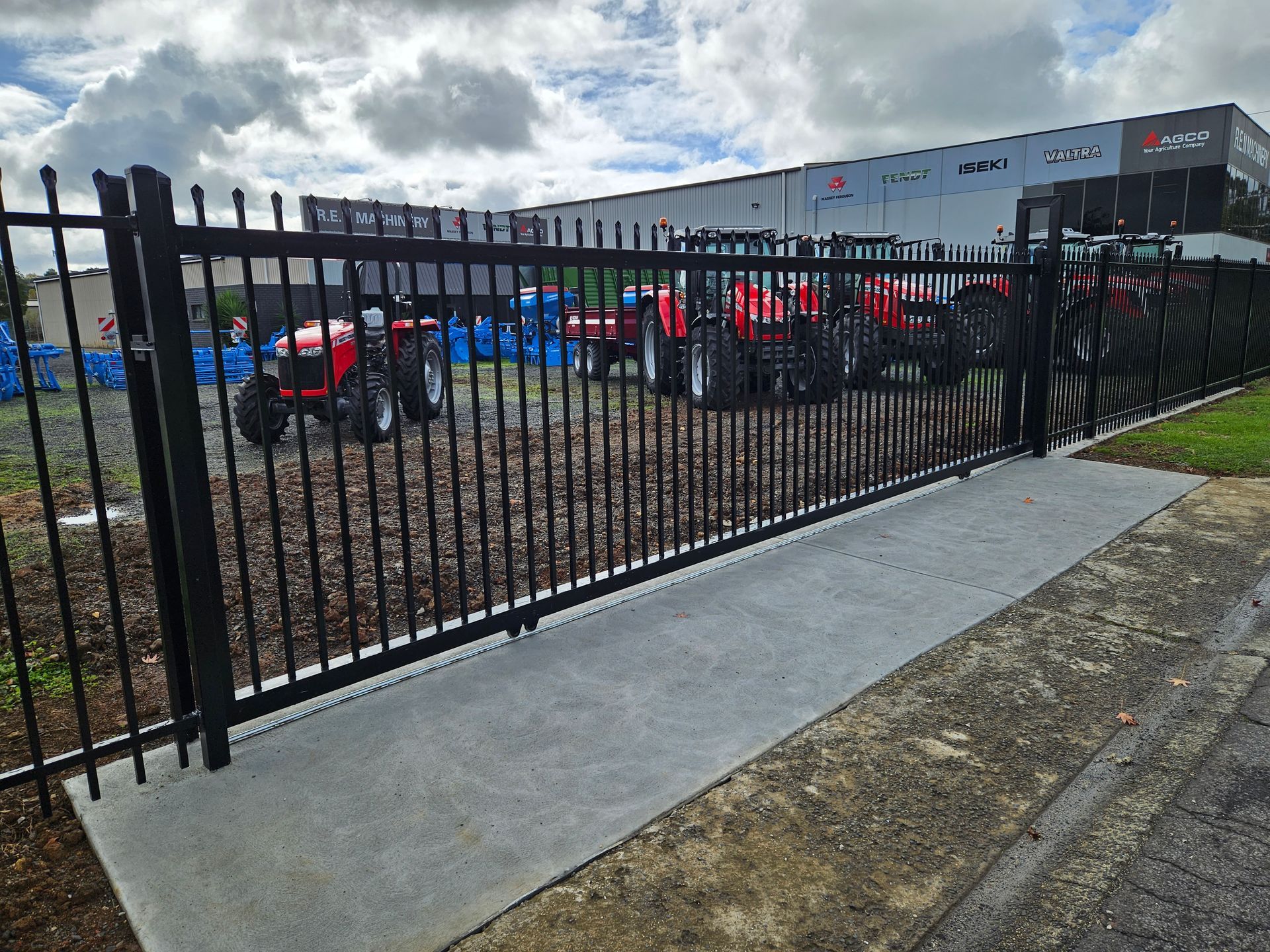 A fence with tractors parked behind it in front of a building.