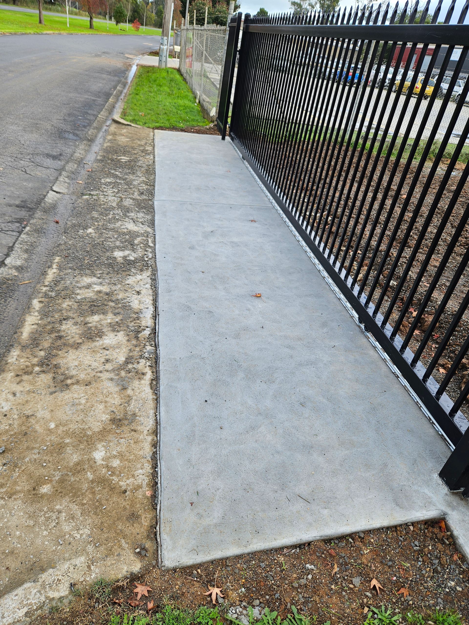 A concrete walkway next to a metal fence on the side of a road.