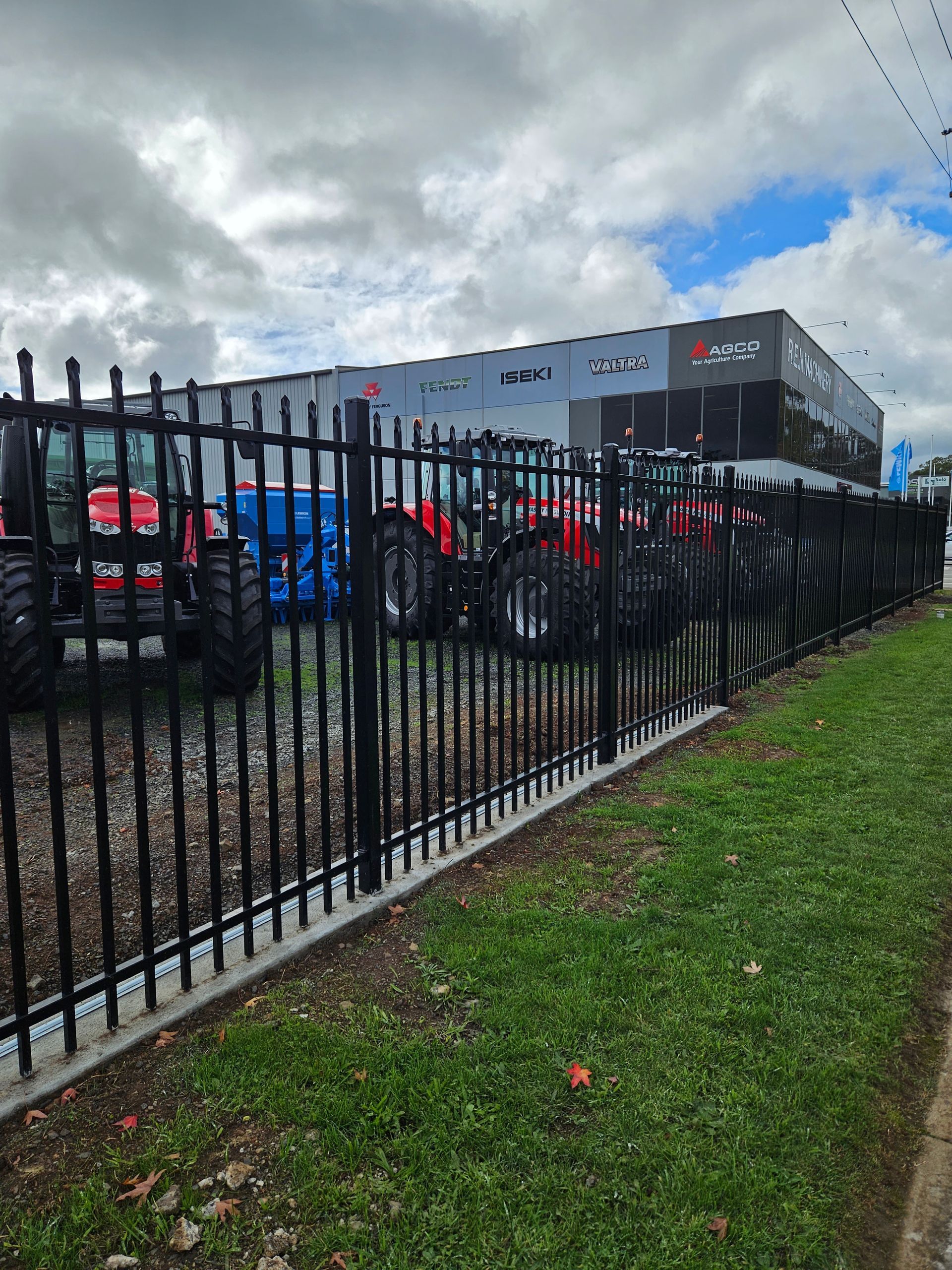 A fence with tractors parked in front of a building.