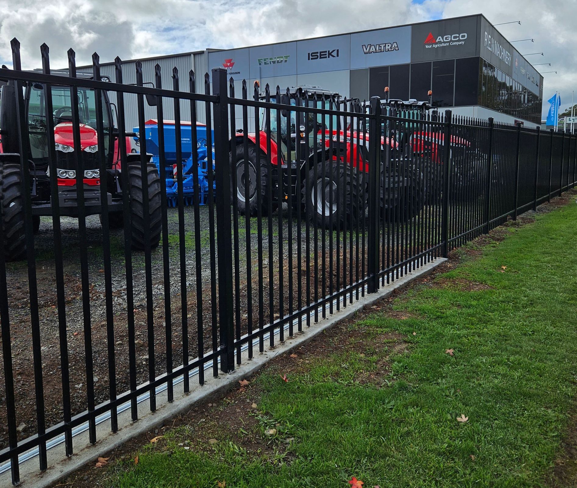 A fence with tractors parked behind it in front of a building.