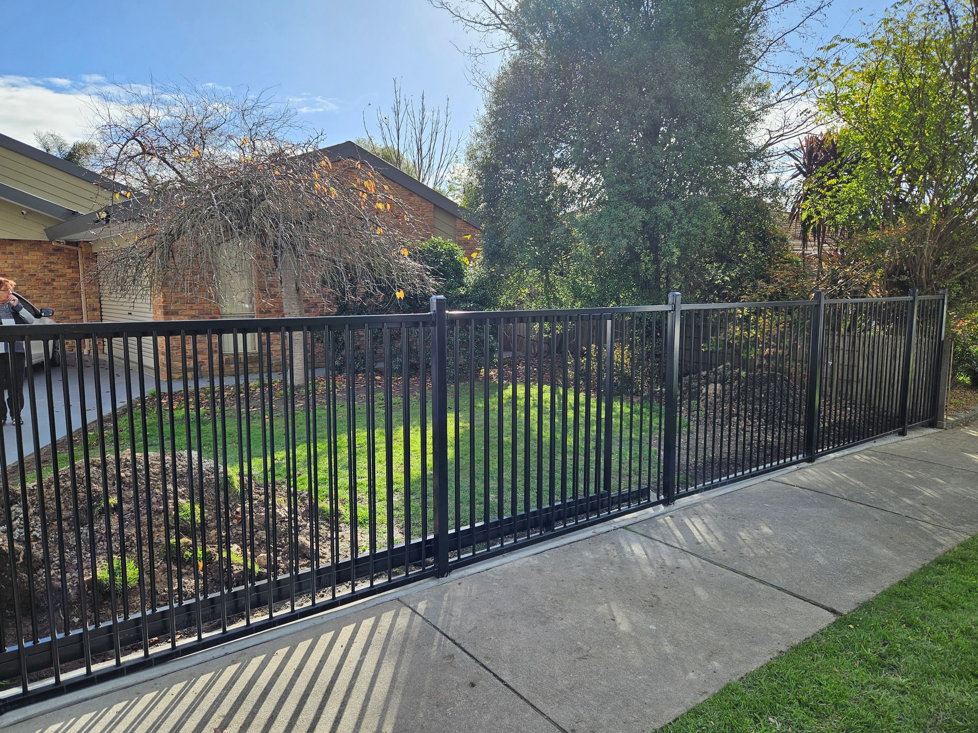 A black fence surrounds a lush green yard in front of a house.