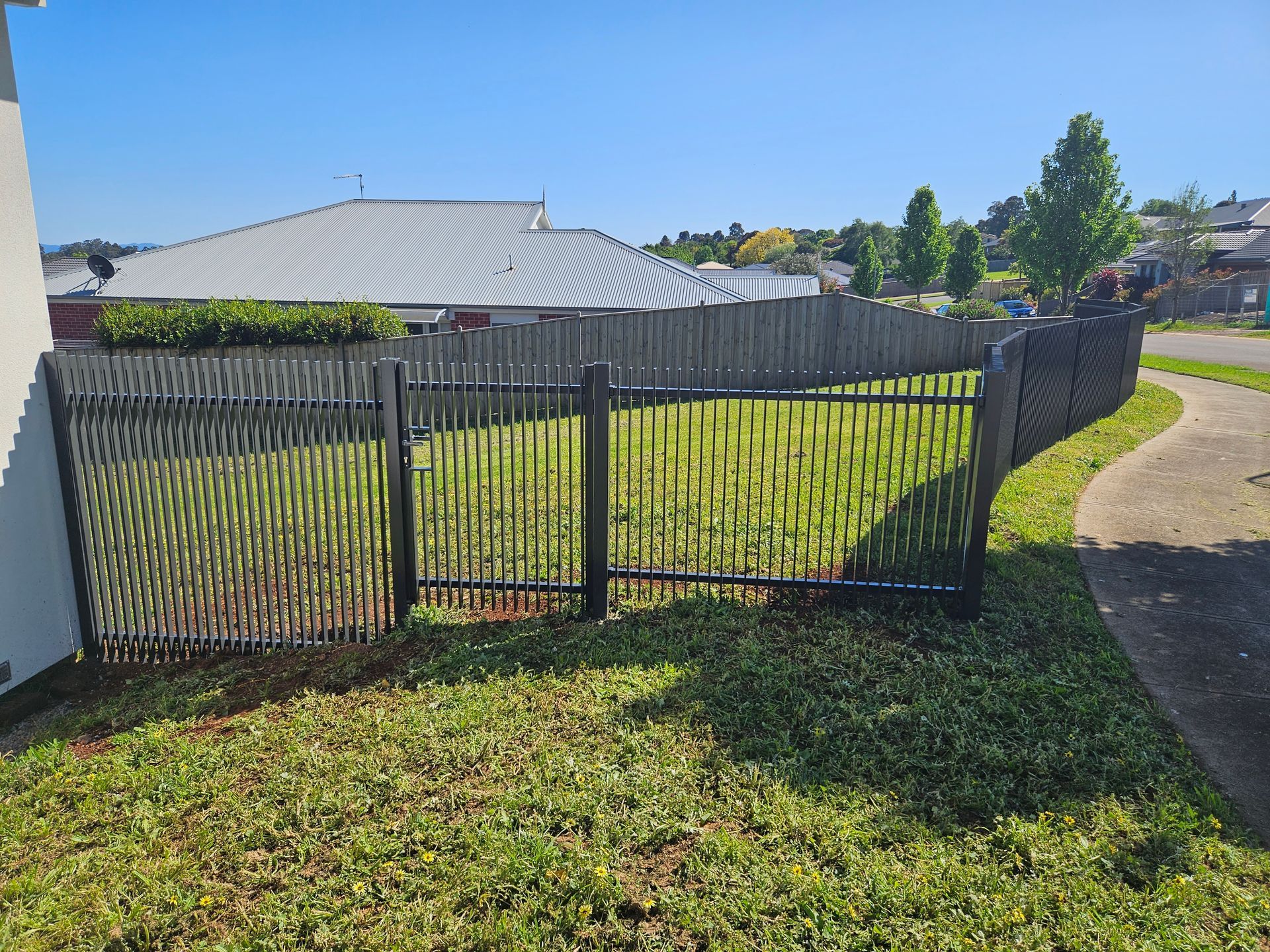 A black fence surrounds a lush green field in front of a house.